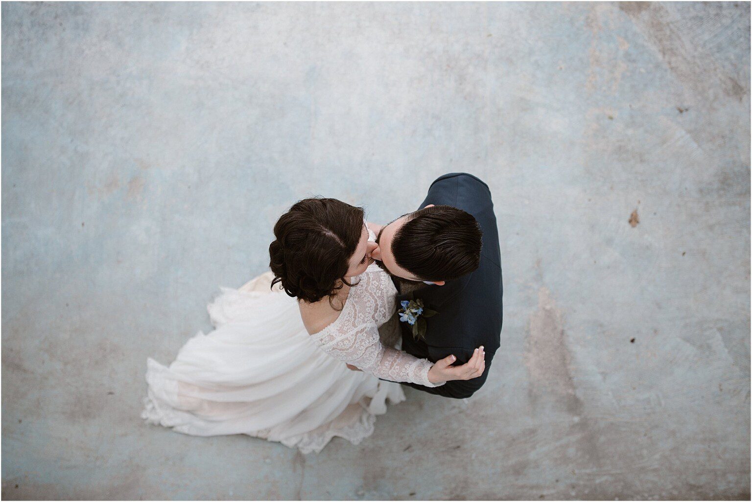overhead photo of bride and groom kissing while standing on blue floor