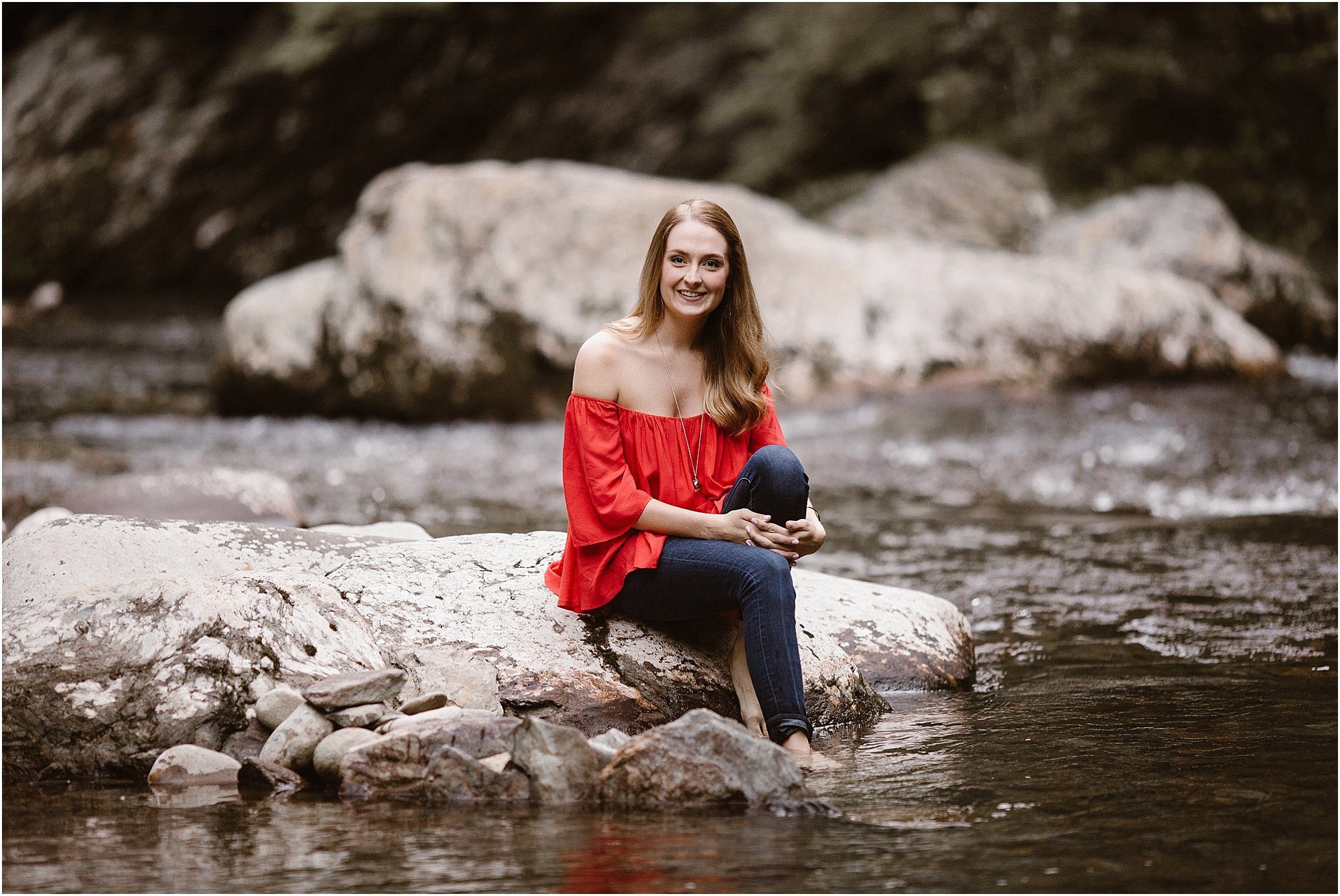 girl in red shirt sitting on rocks with feet in river