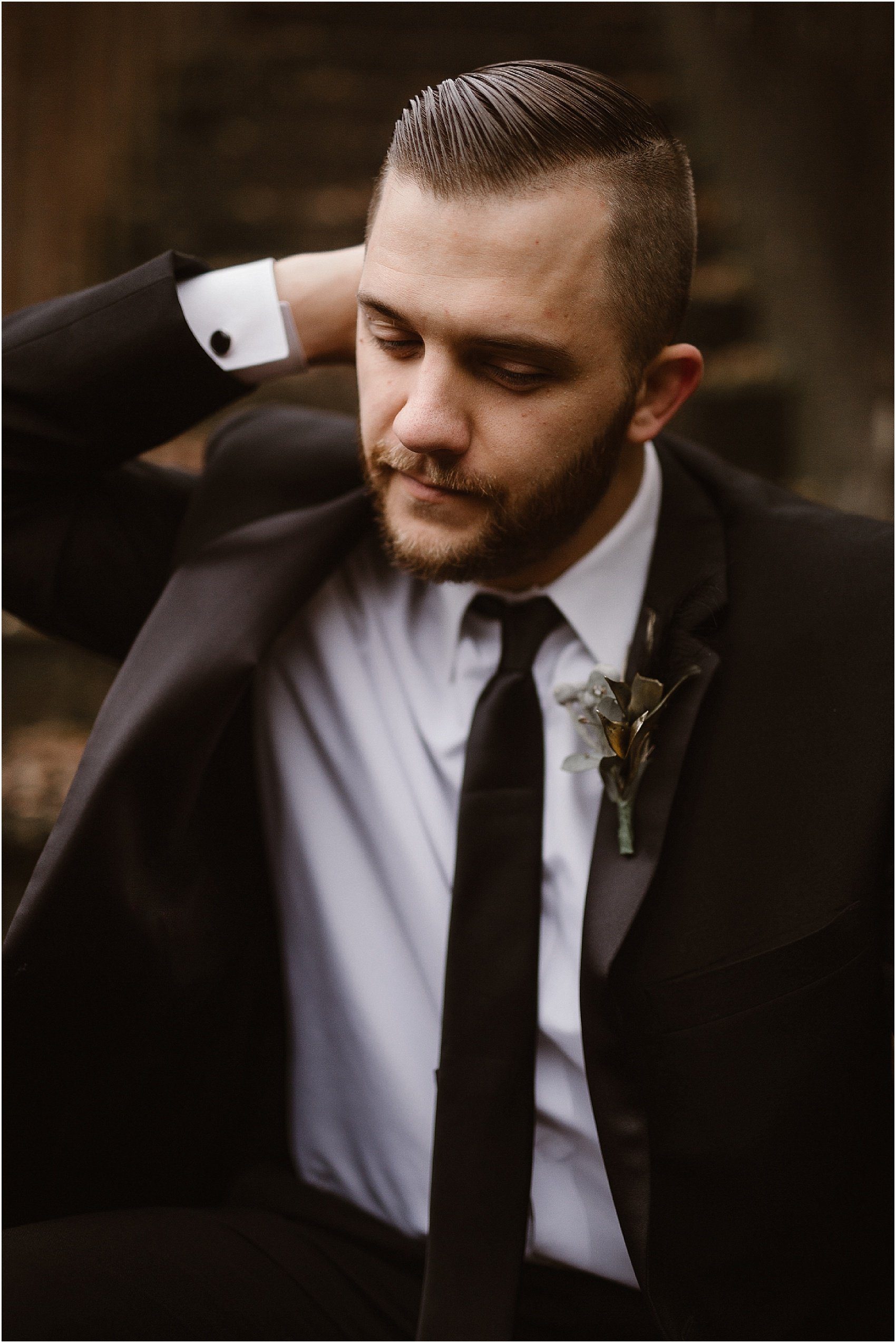 man swoops hand through hair while wearing black wedding suit with boutonniere 