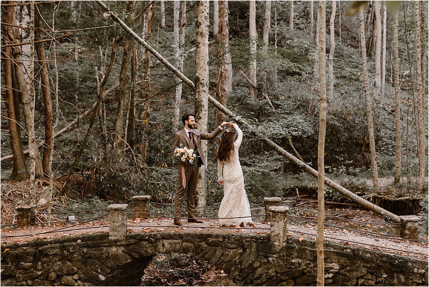 man twirls woman in long white wedding dress on top of stone bridge in the forest 