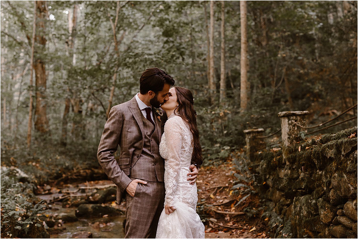 man and woman kiss next to stone bridge in forest fall setting
