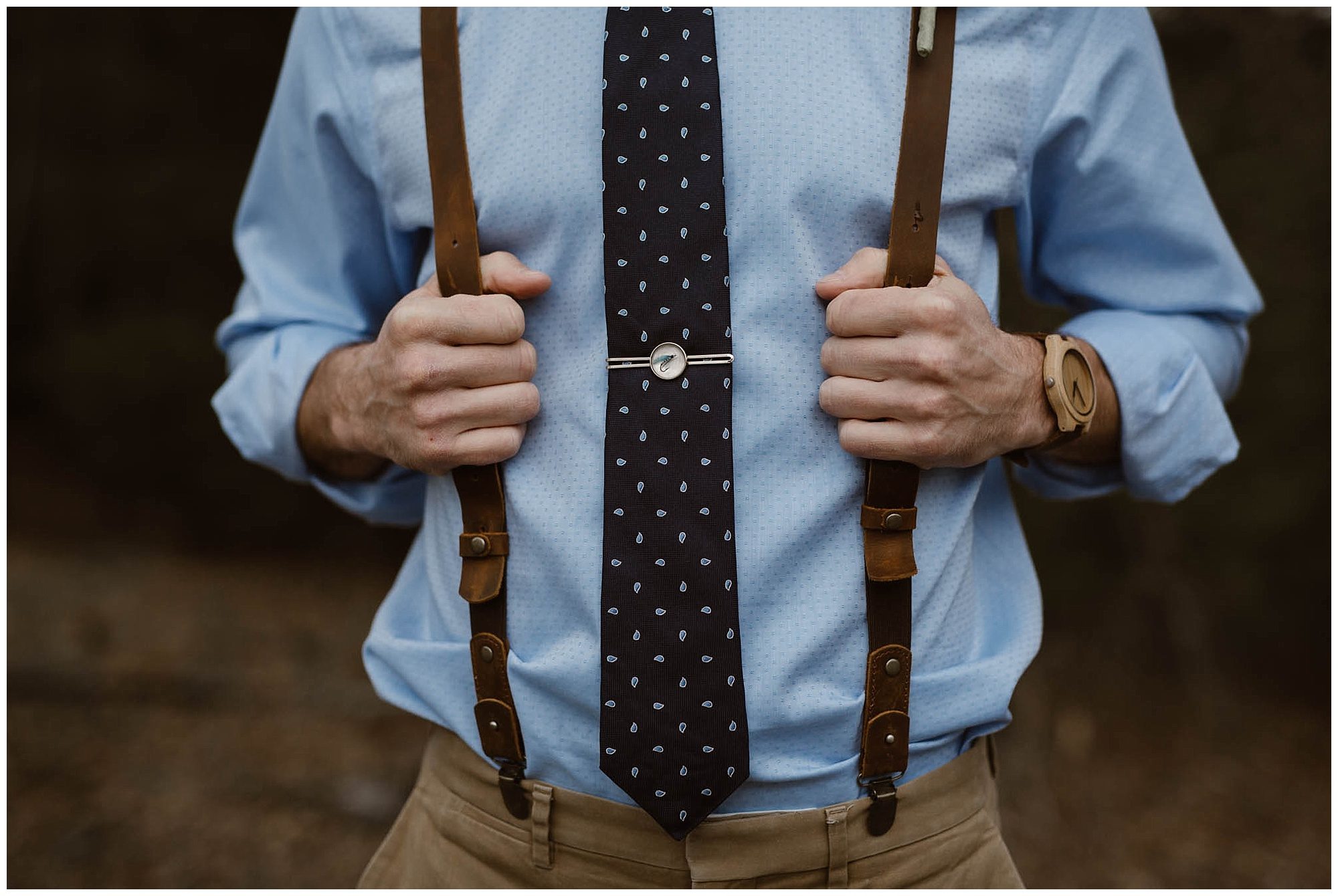 man holding leather suspenders while wearing blue shirt