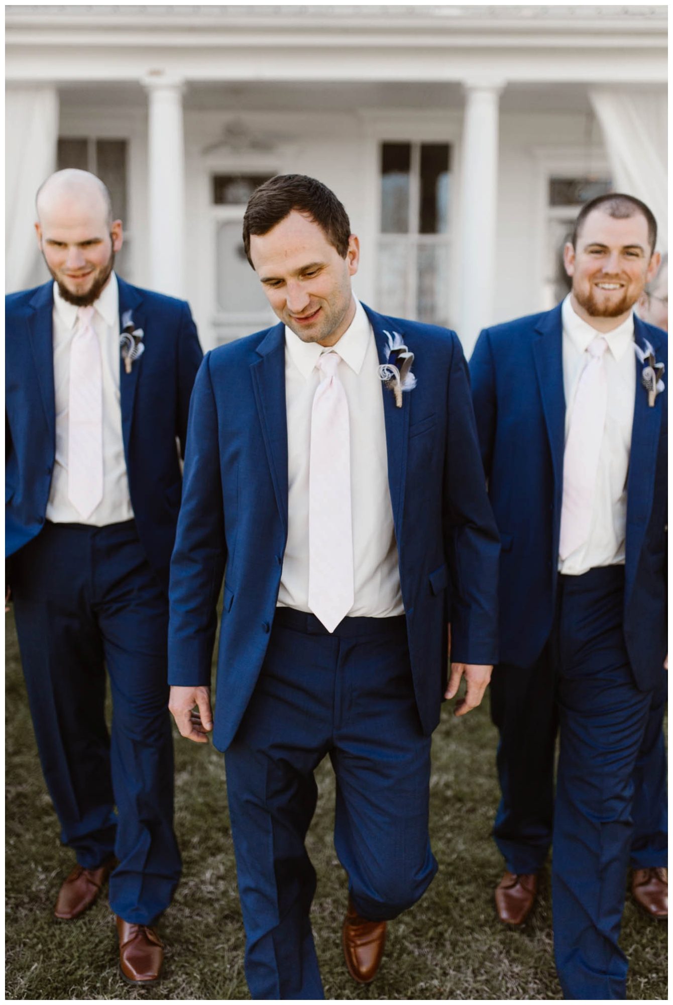 groom and groomsmen with feather boutonnieres walking outside of white house