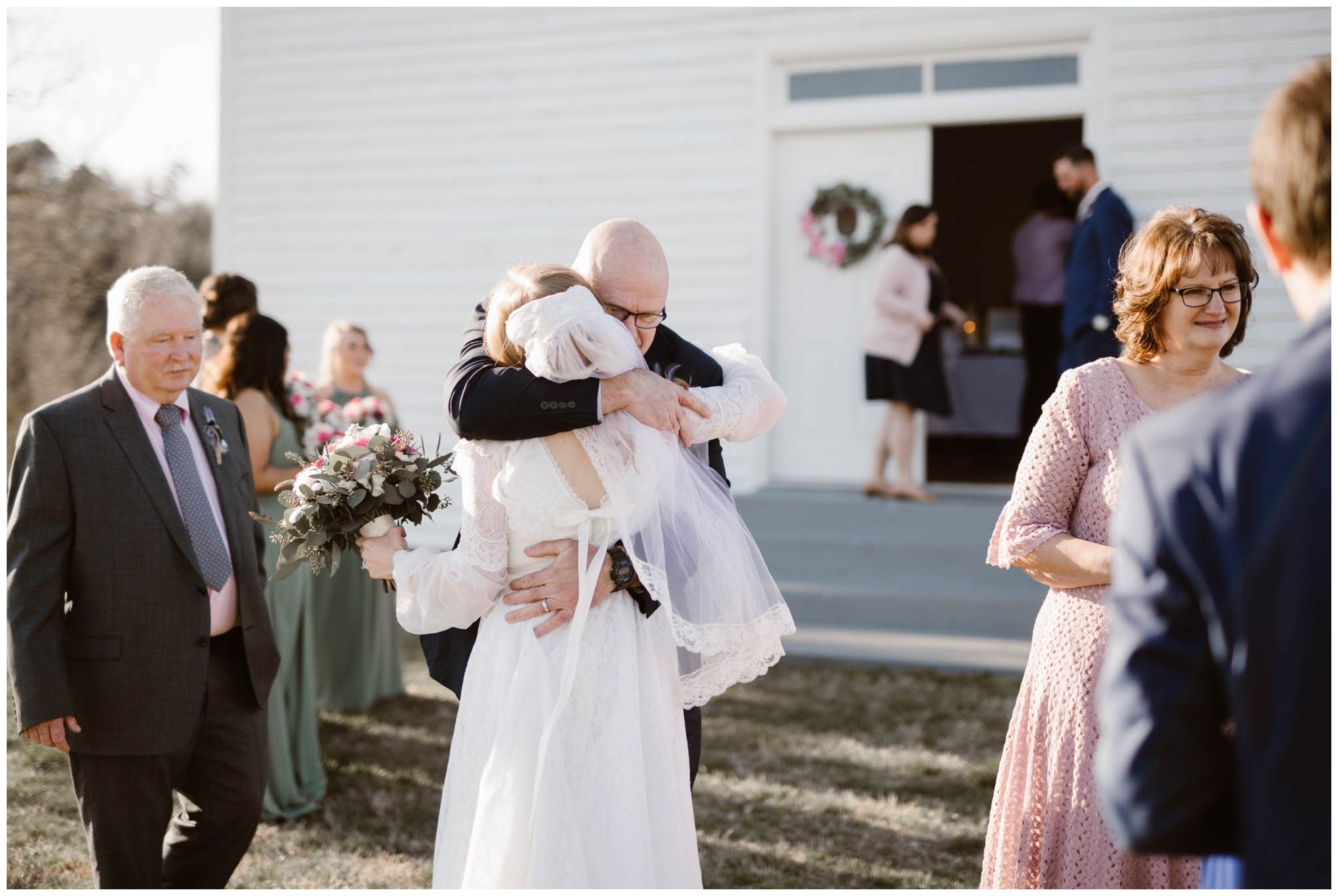 bride hugging priest outside of church on wedding day