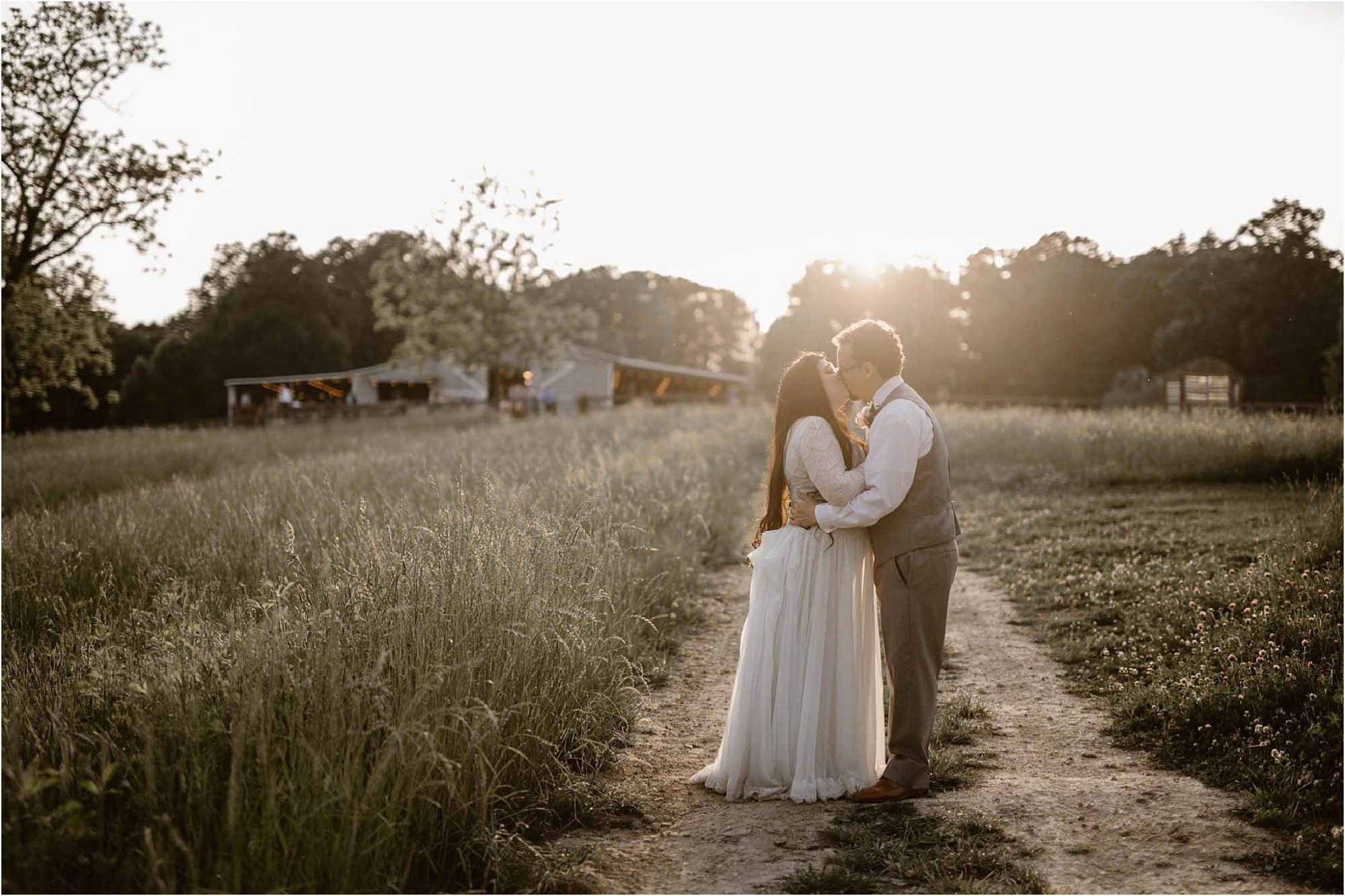 bride and groom kissing in field at sunset
