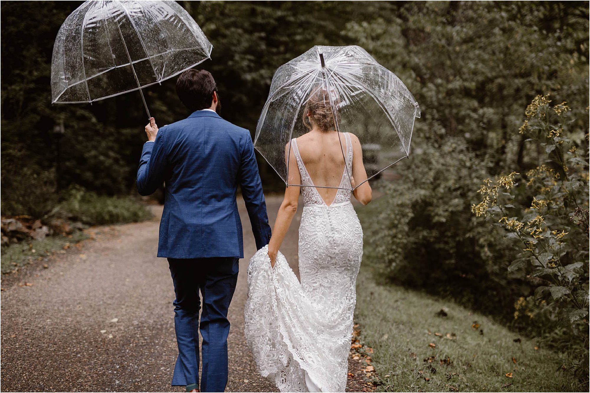 bride and groom walking with clear umbrellas on rainy wedding day