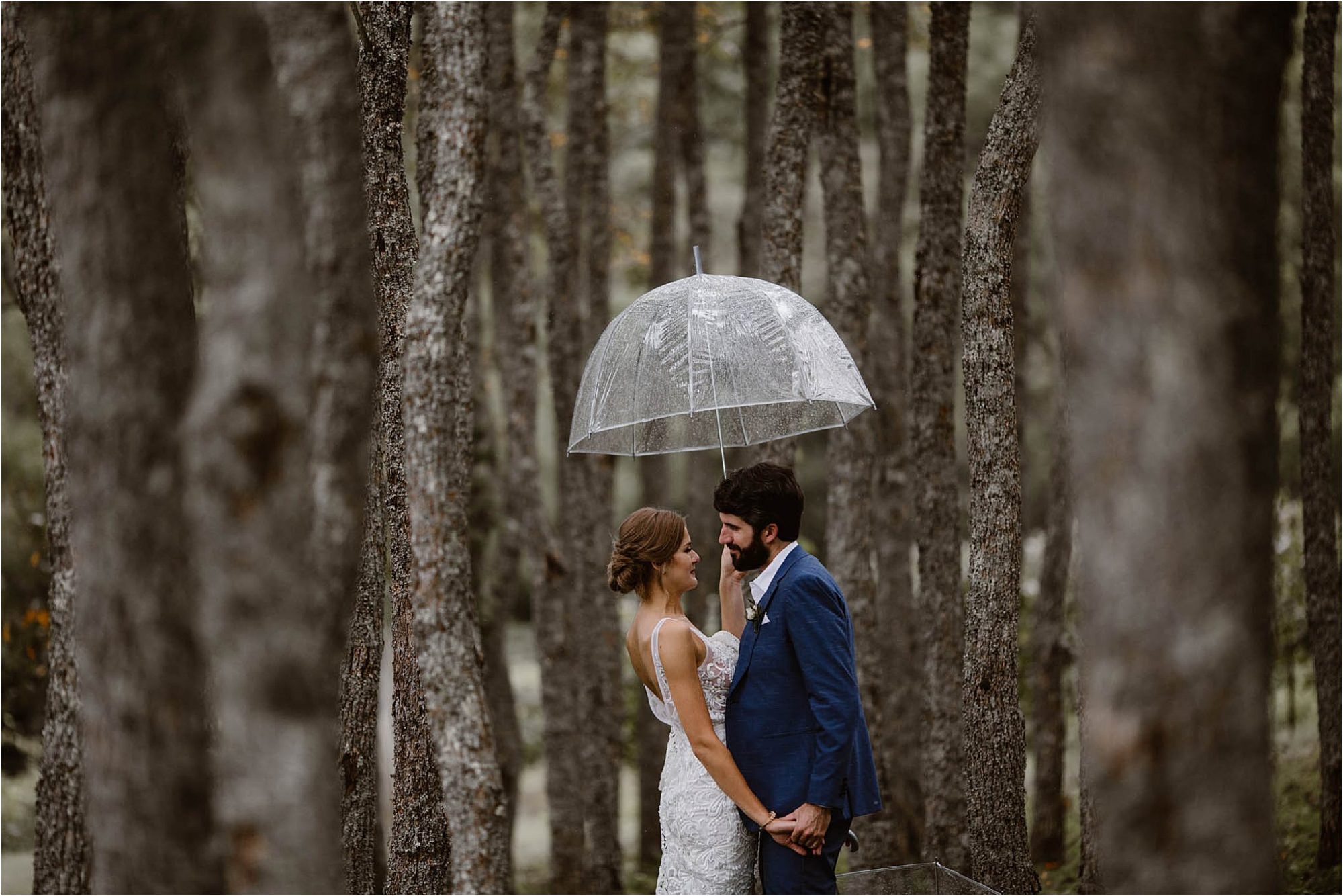 bride and groom standing in woods with umbrella