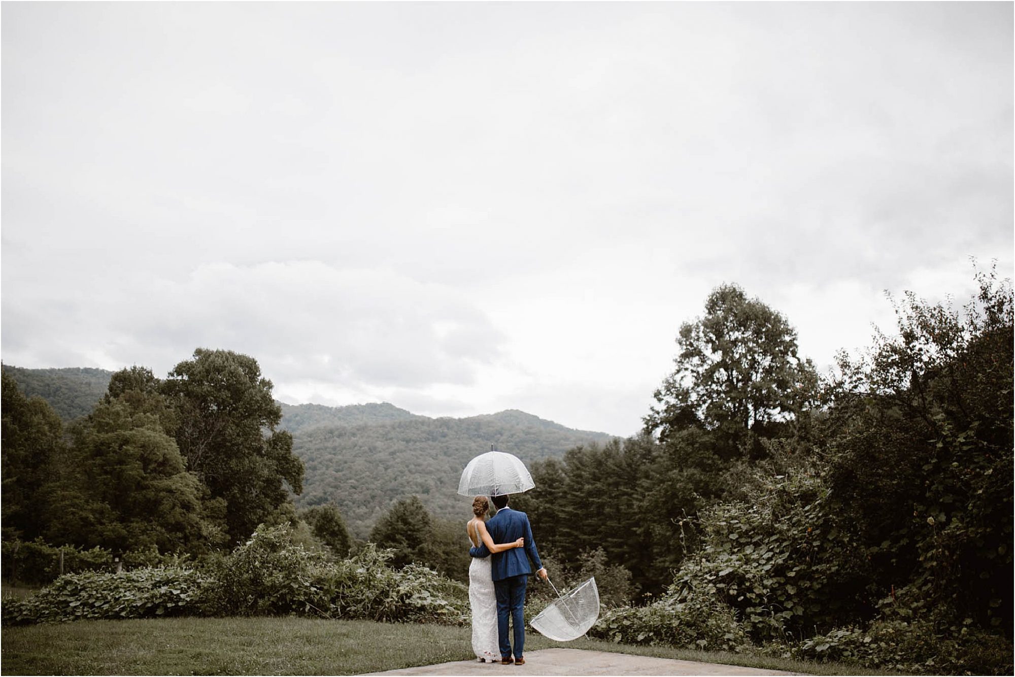 bride and groom holding umbrellas looking at mountains at Vineyards at Betty's Creek
