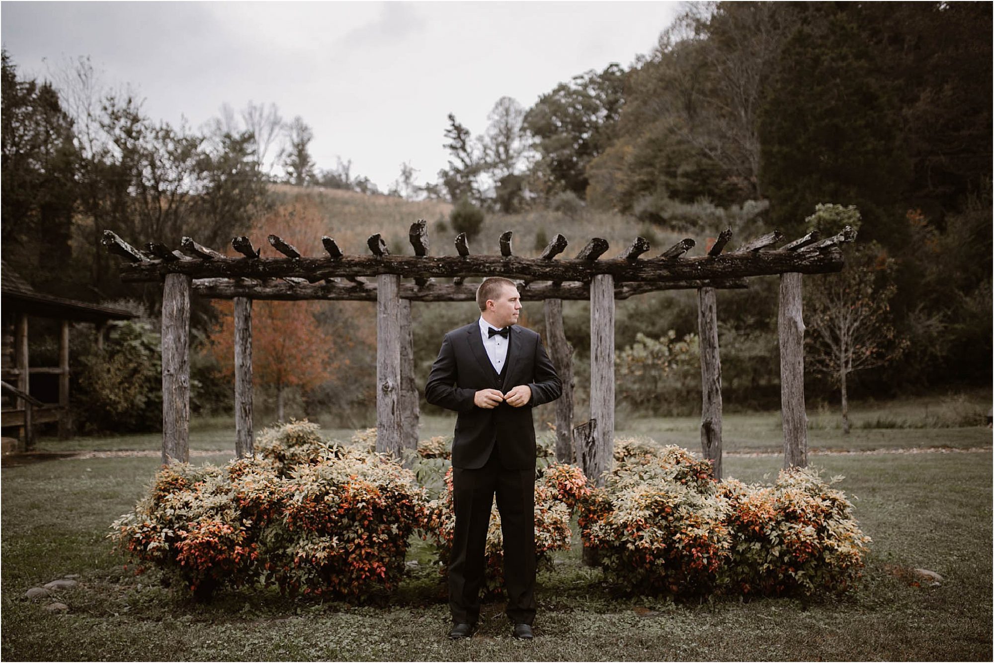 groom in black suit standing in field at Pure Water Farm