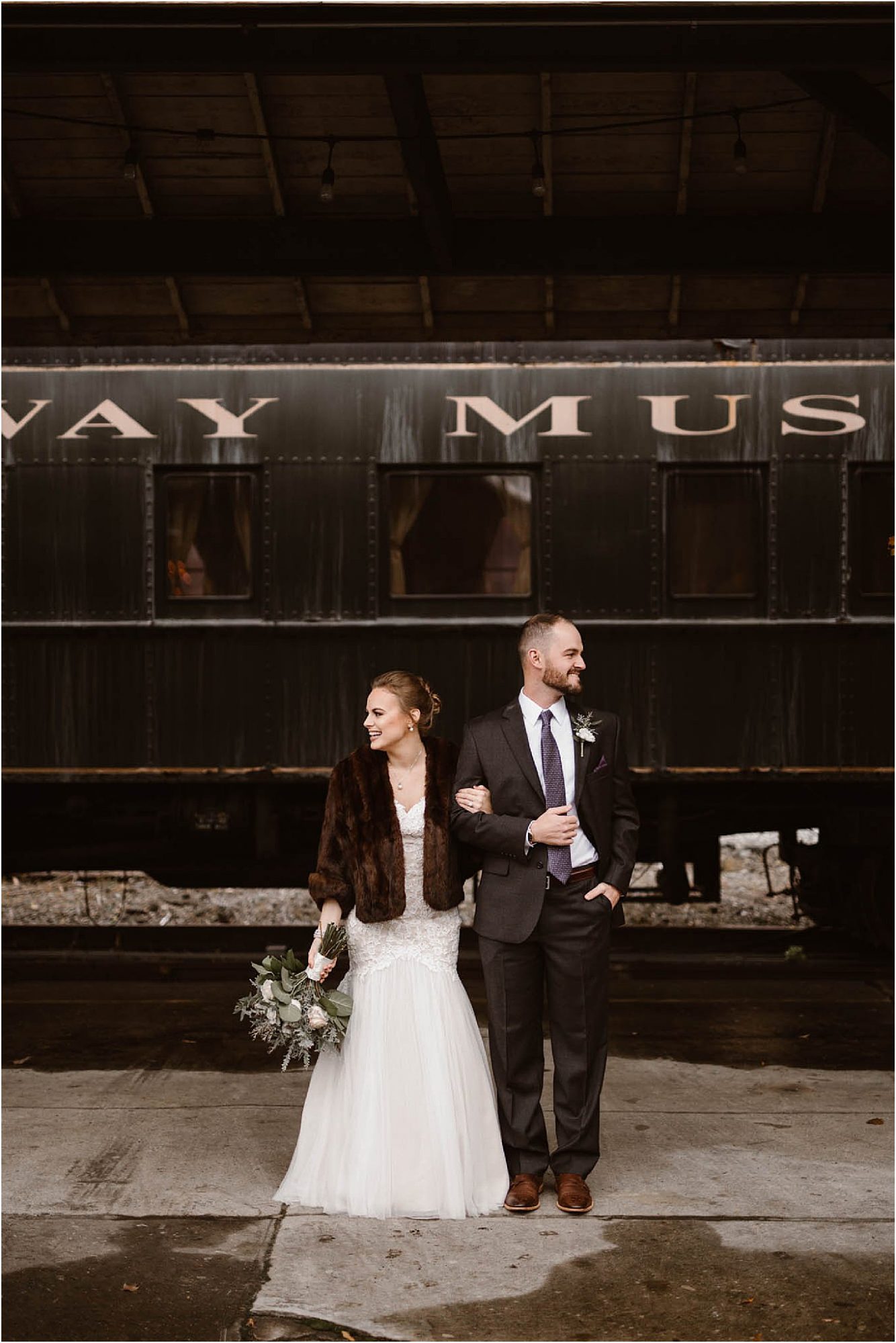 bride in faux fur jacket standing next to groom next to train