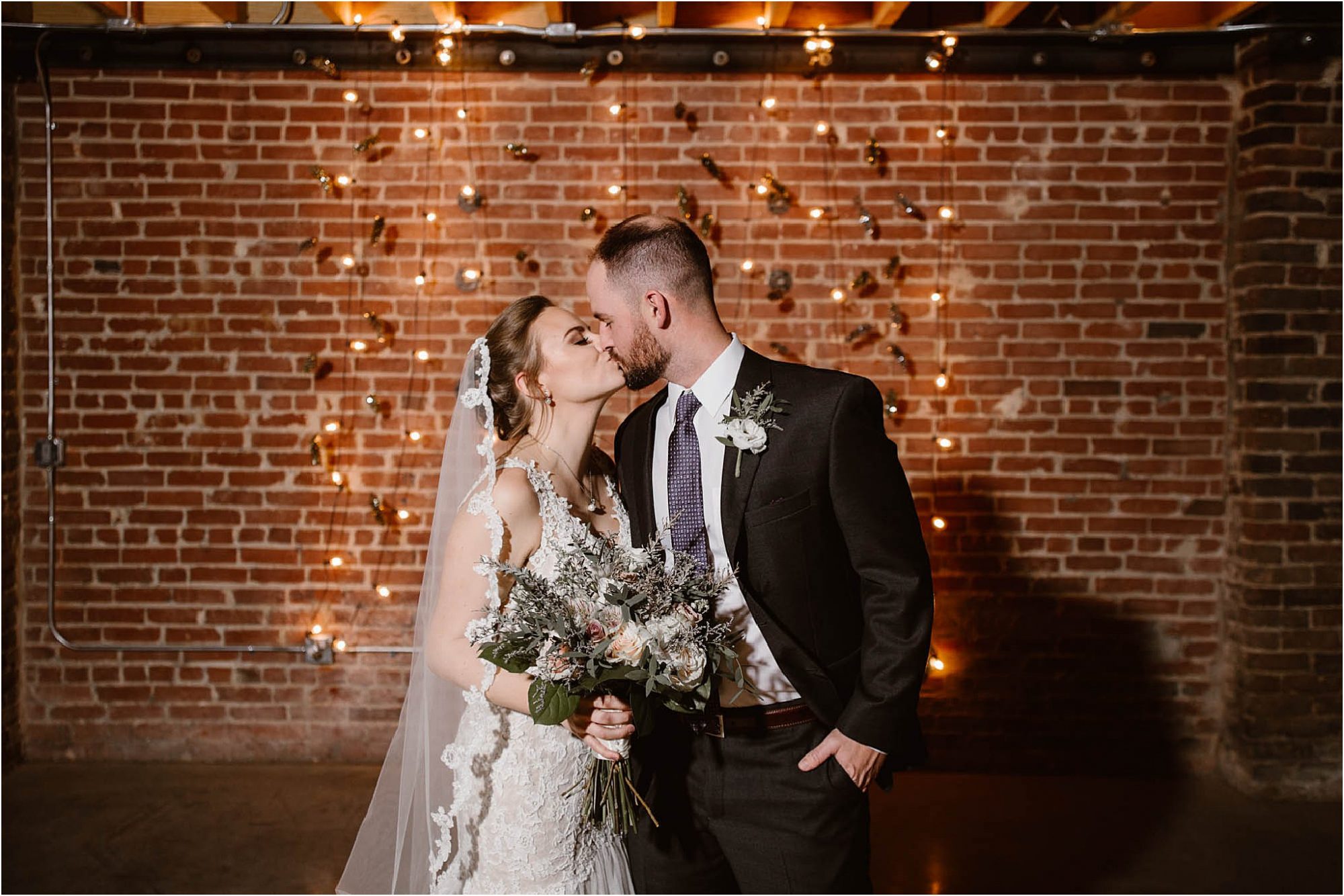 bride and groom kissing in front of wall of lights