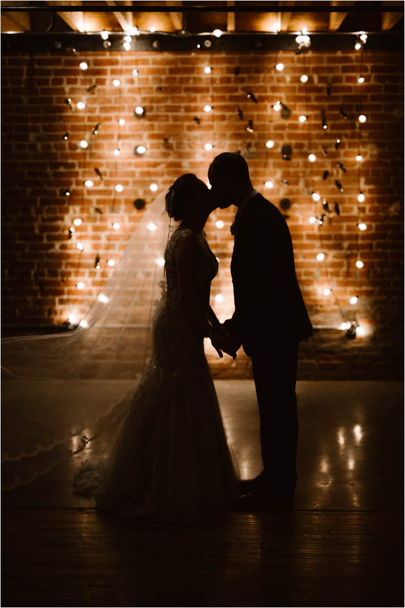 silhouette of bride and groom kissing in front of wall of lights