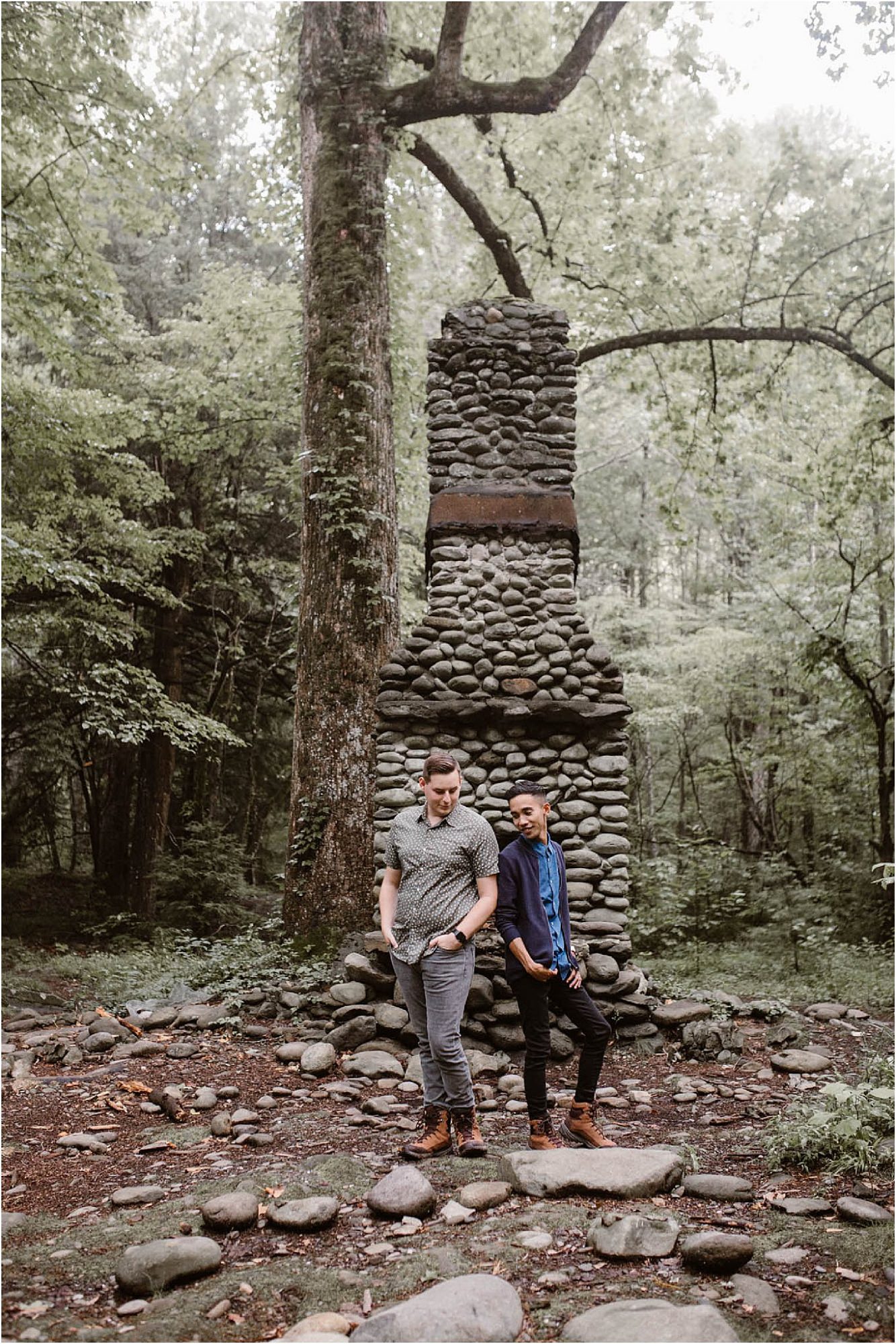 two men standing back to back in front of chimney stack in forest