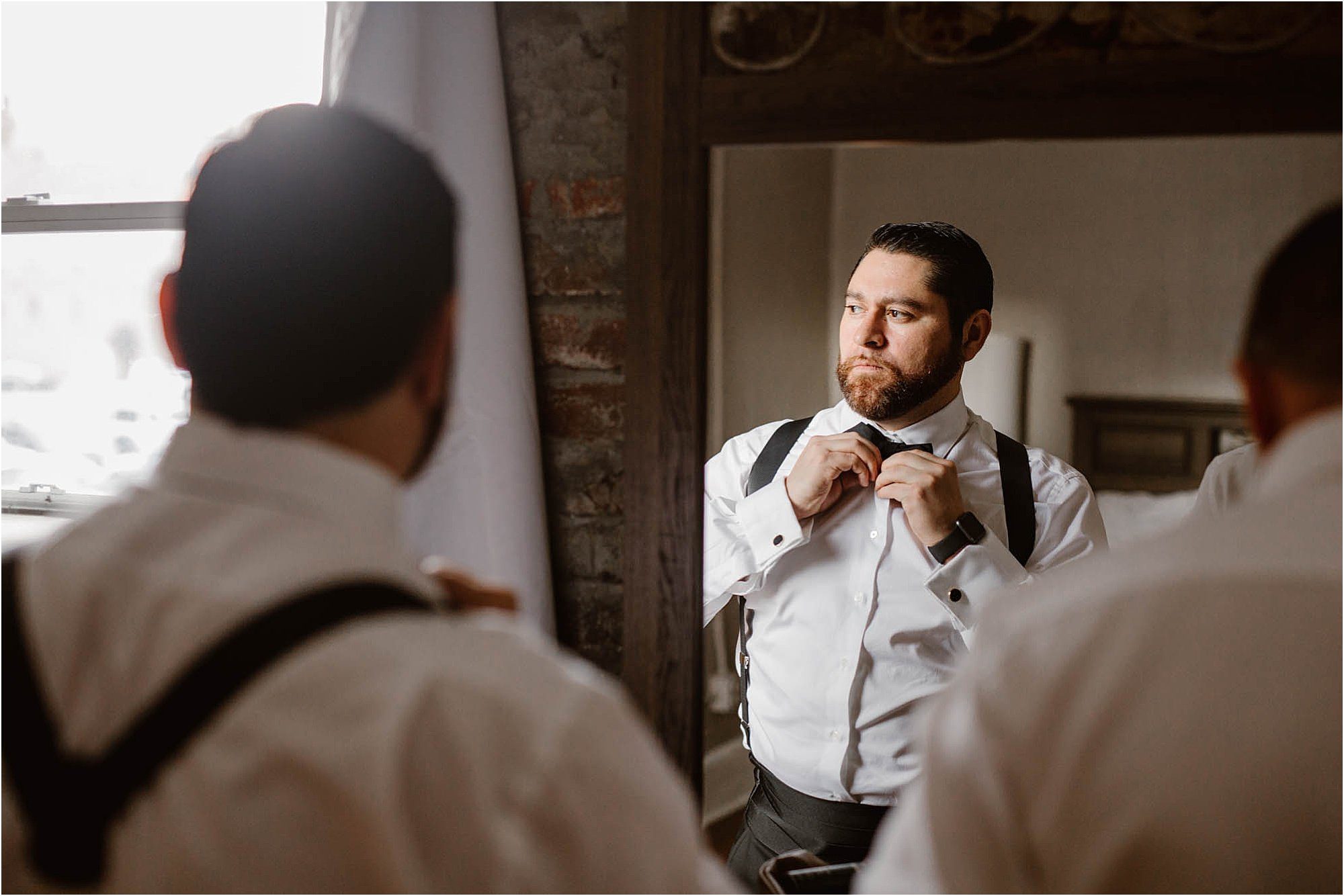 groom putting on bow tie in mirror
