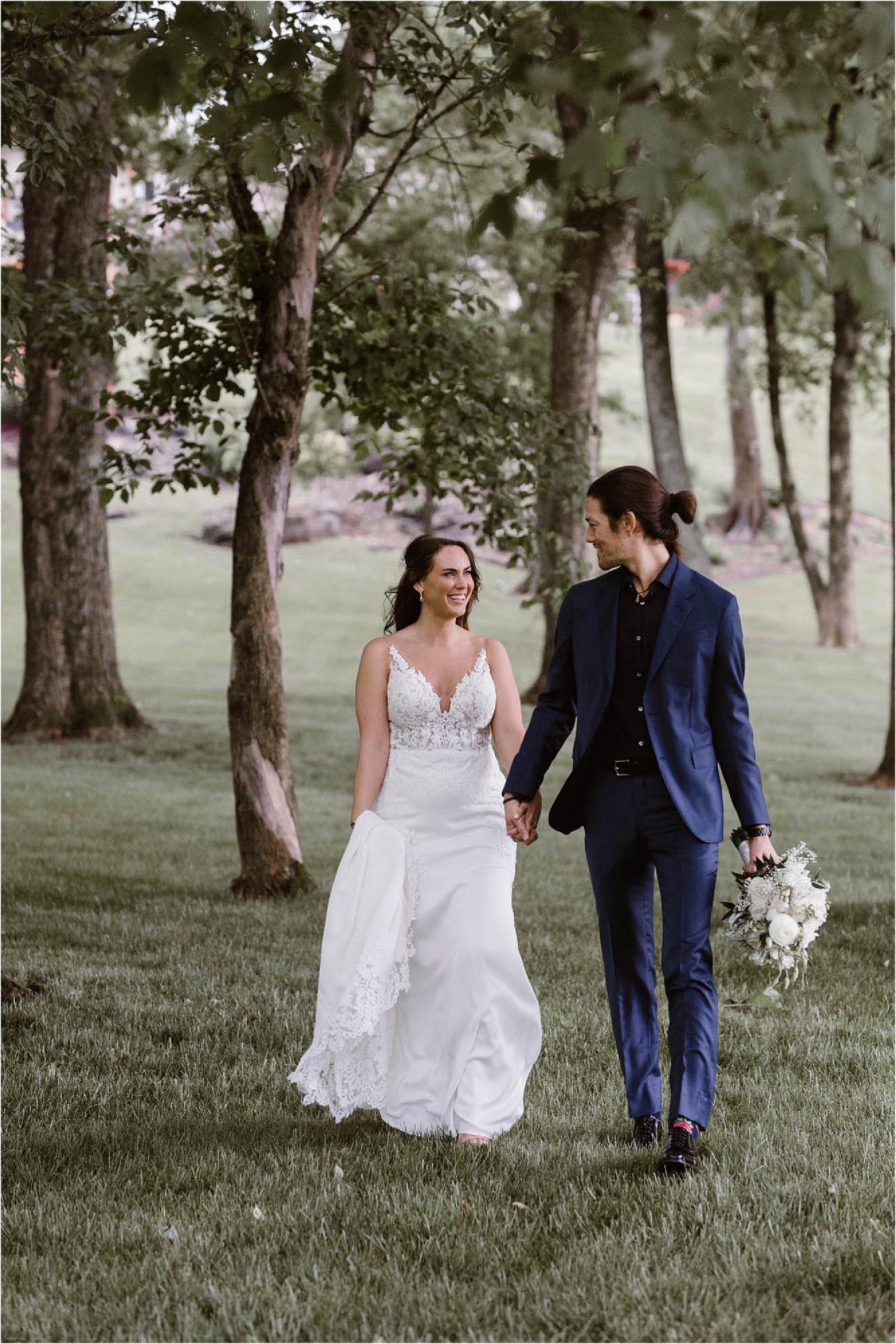 bride and groom walking between trees in backyard wedding