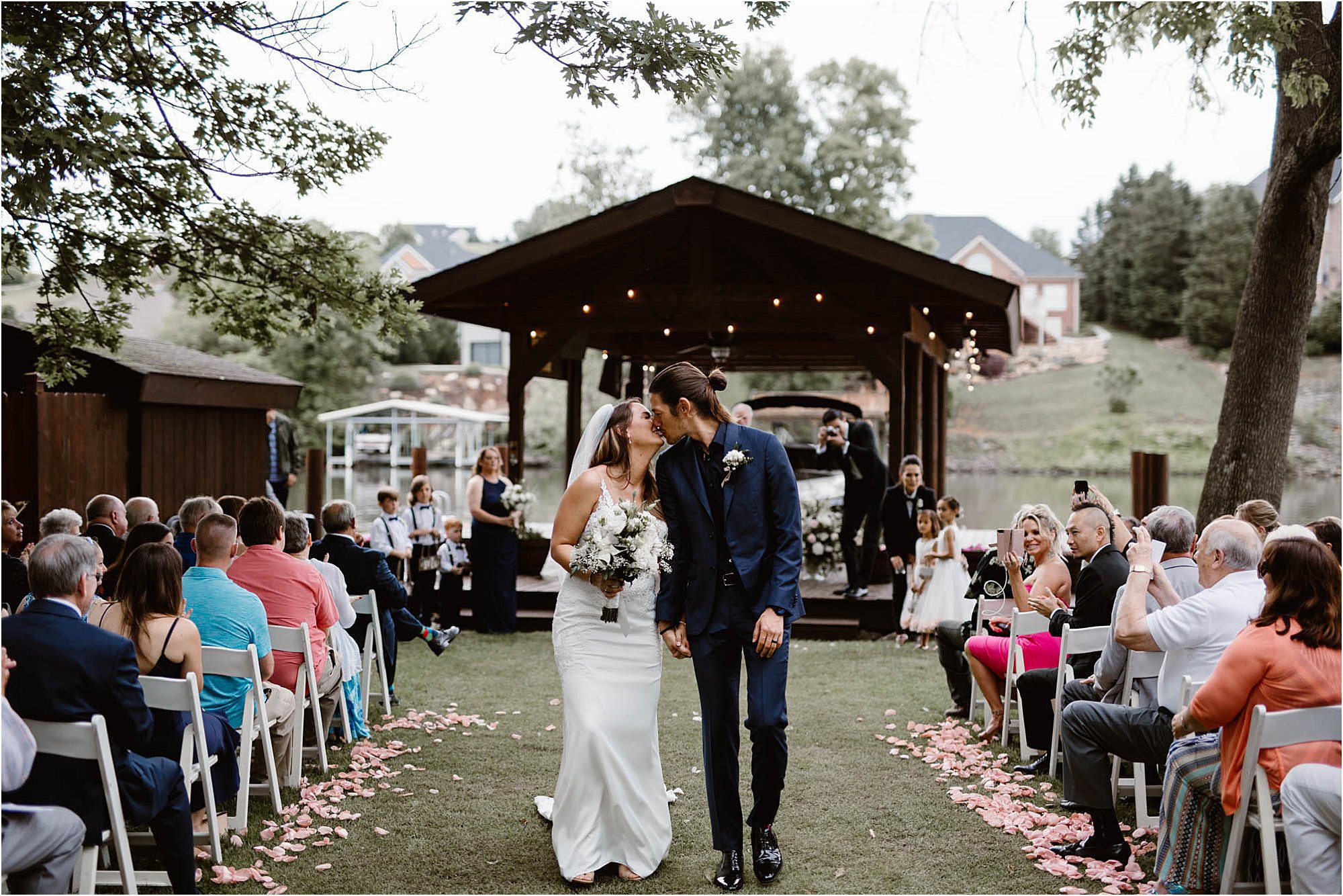 bride and groom kissing while walking down aisle at backyard wedding ceremony