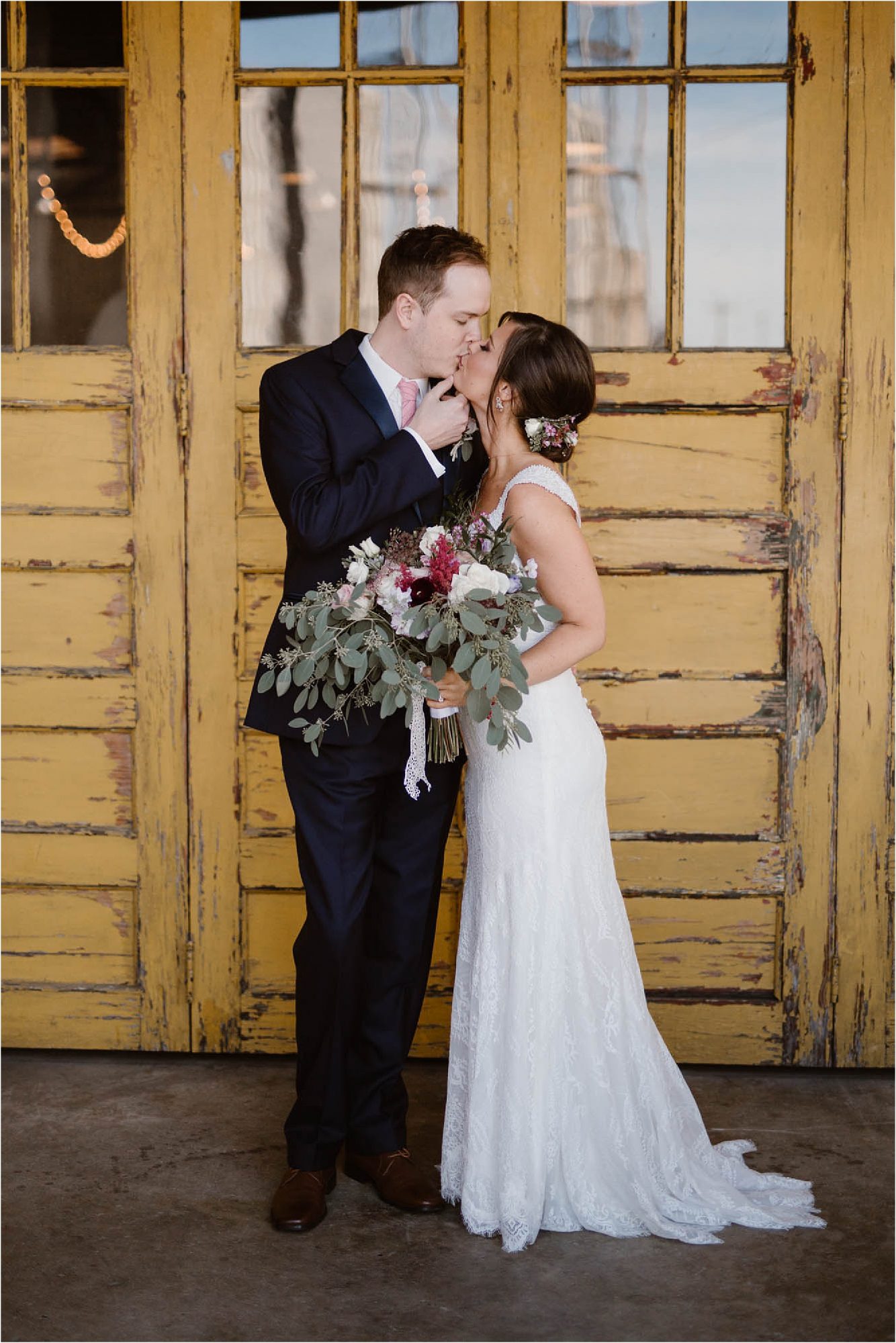bride and groom kissing in front of yellow door