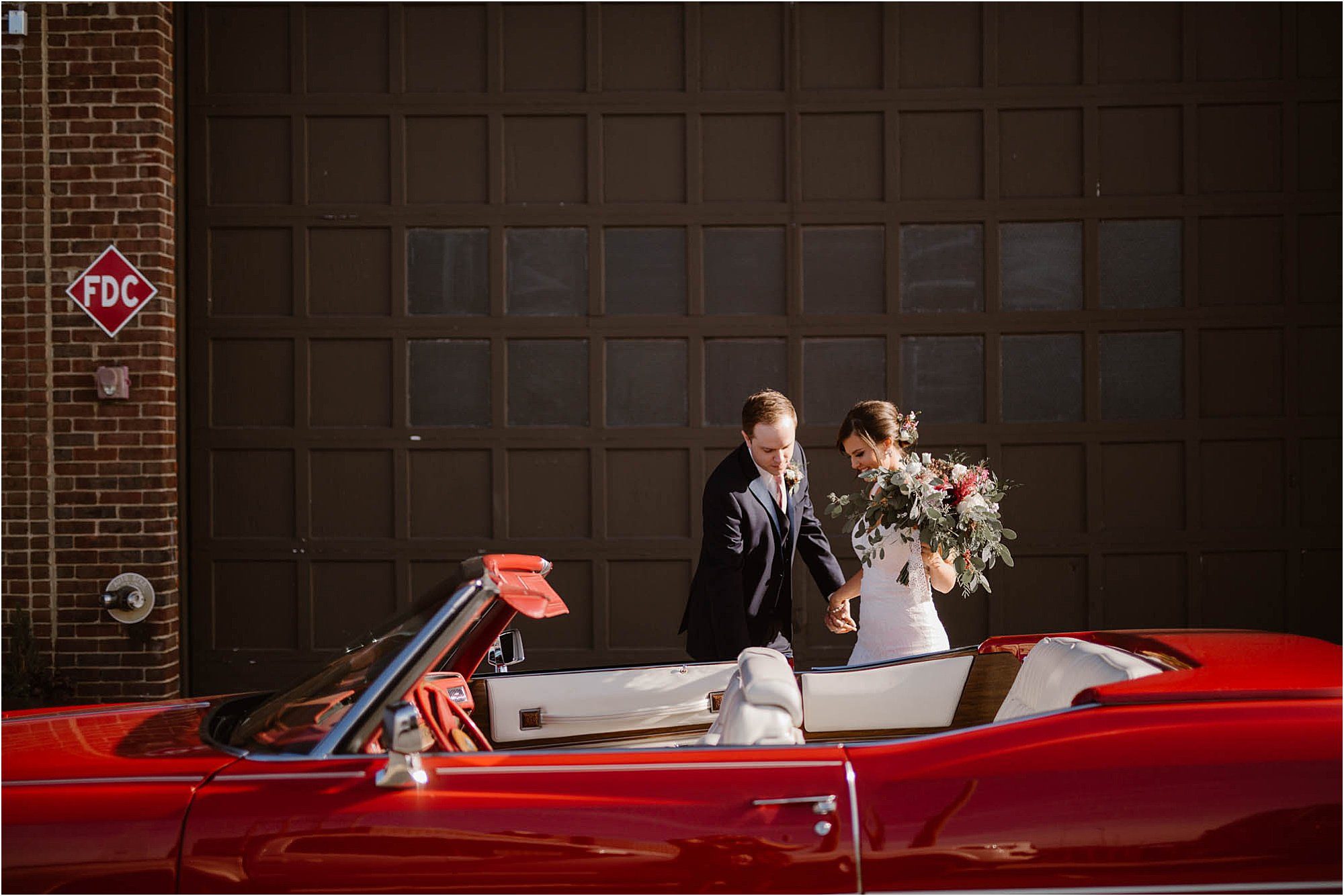 groom helping bride into red convertible
