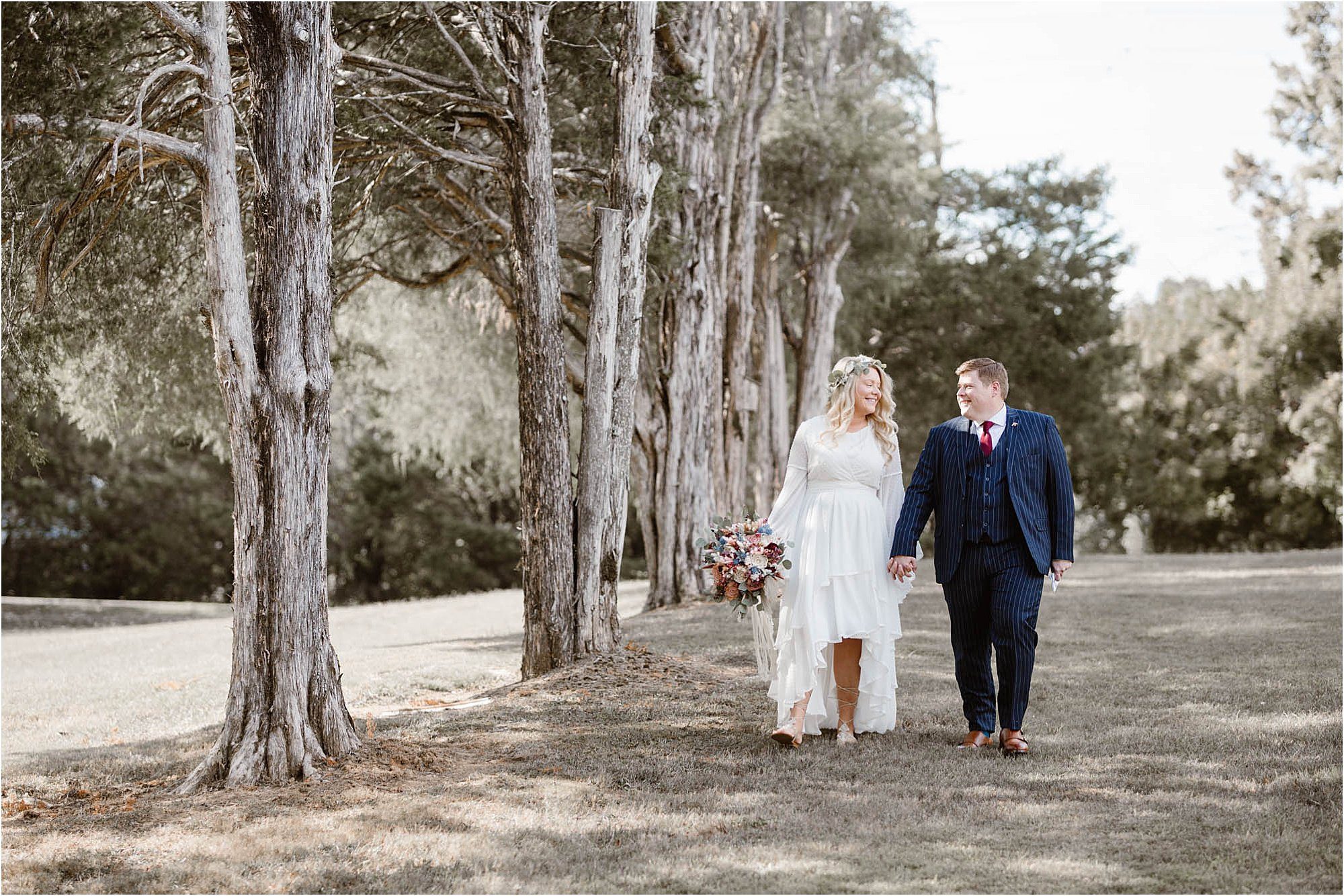 bride and groom walking along tree line
