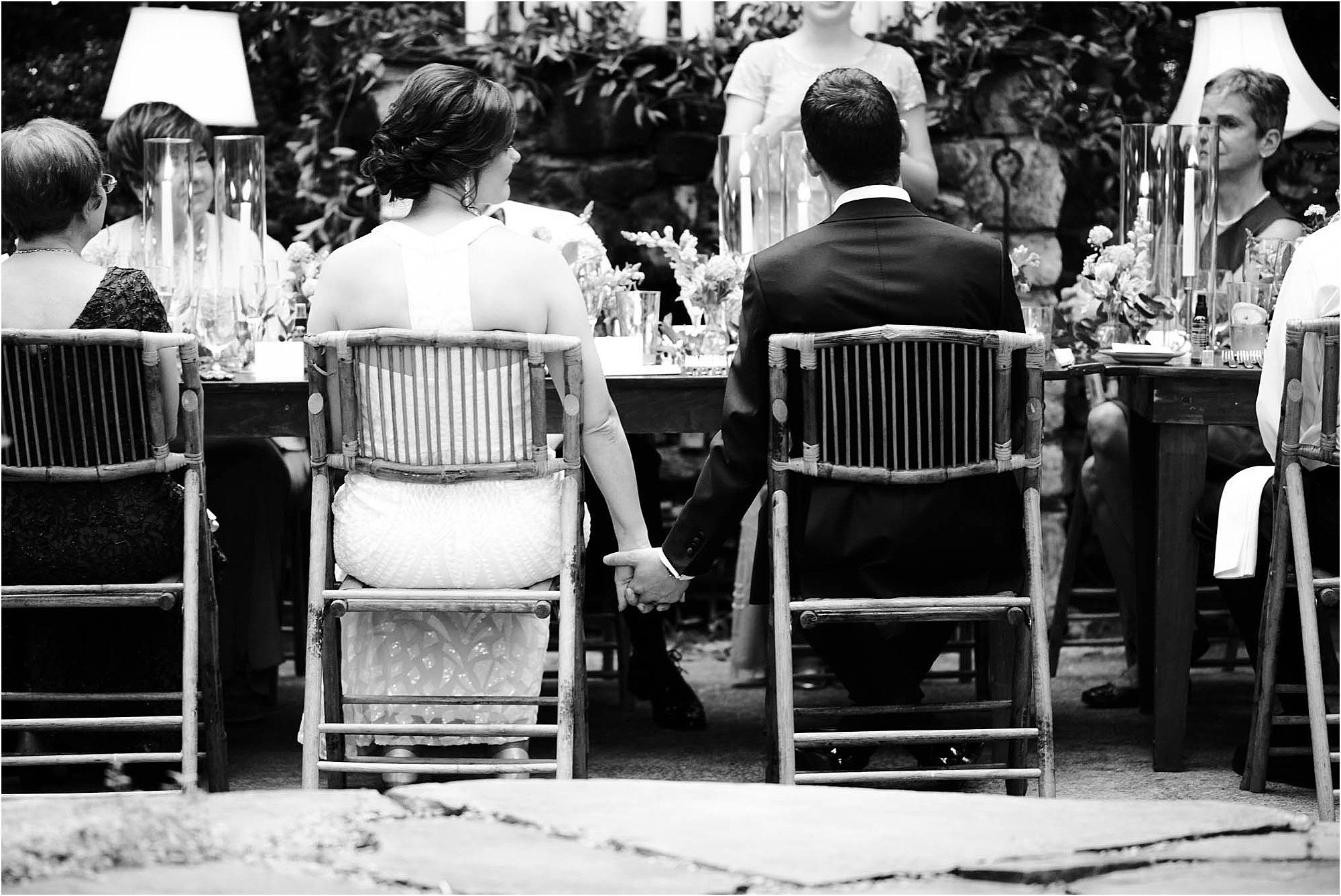 bride and groom hold hands at table at wedding.