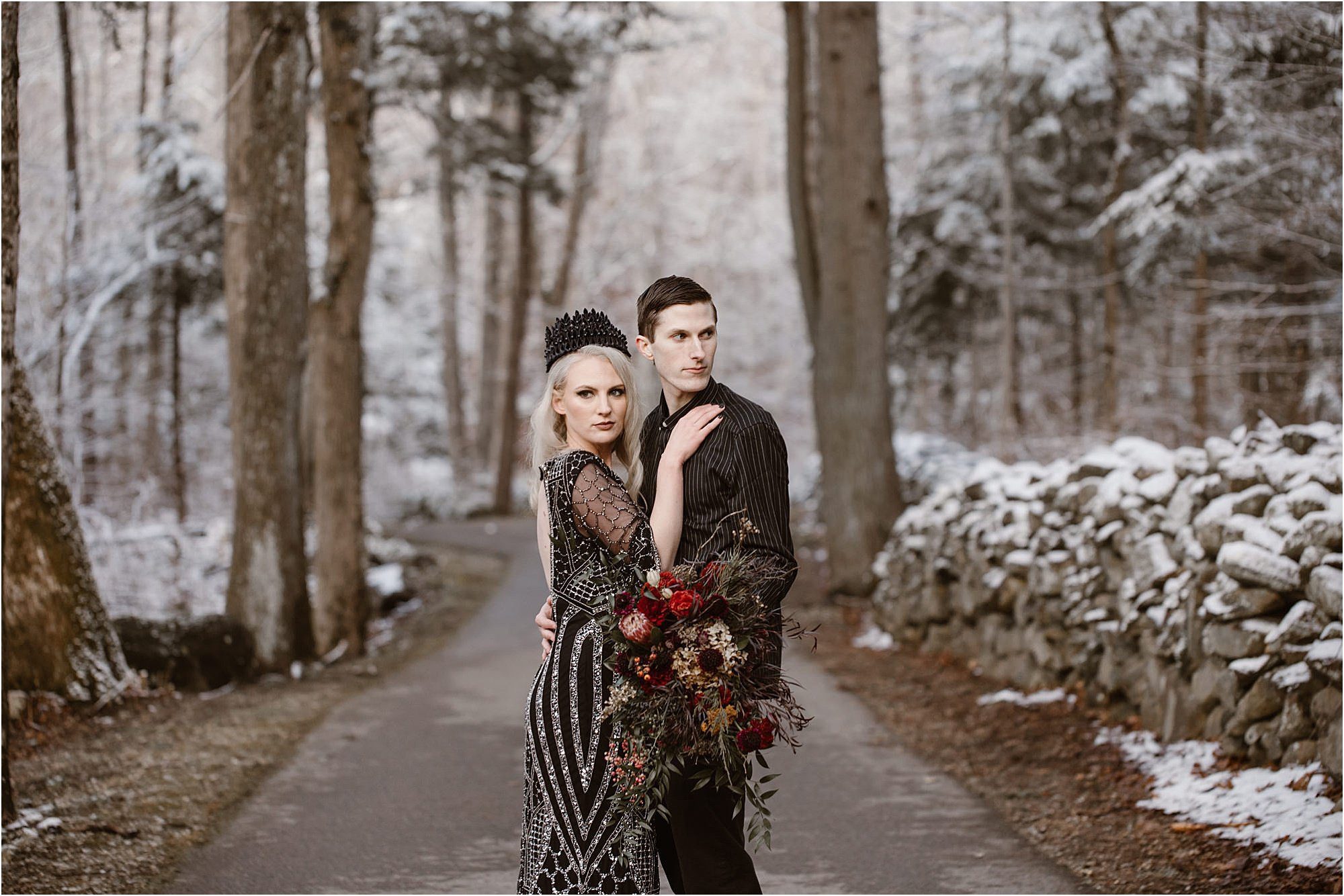 bride and groom in black wedding outfits standing in road in forest