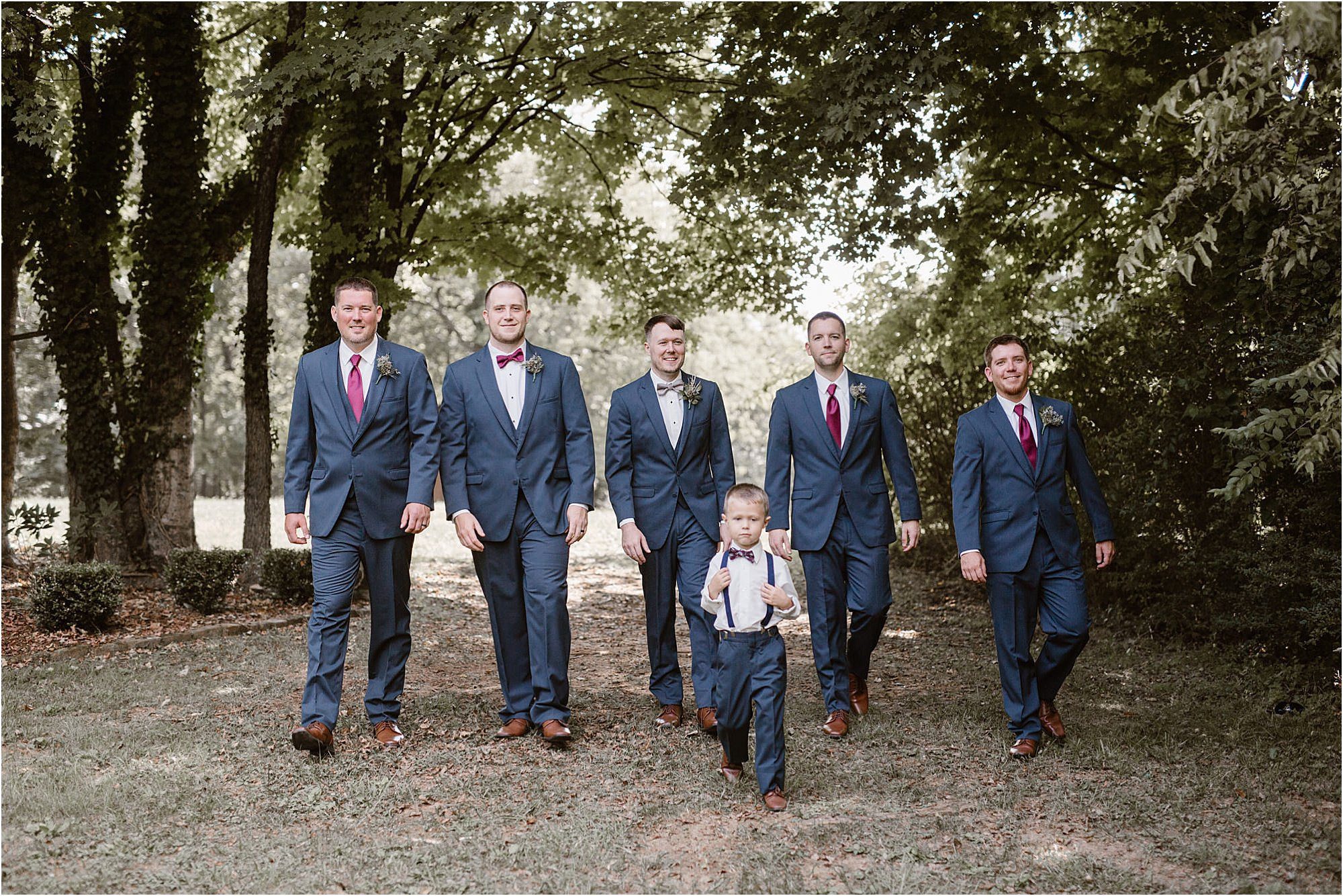 ring bearer walking with groomsmen in blue suits