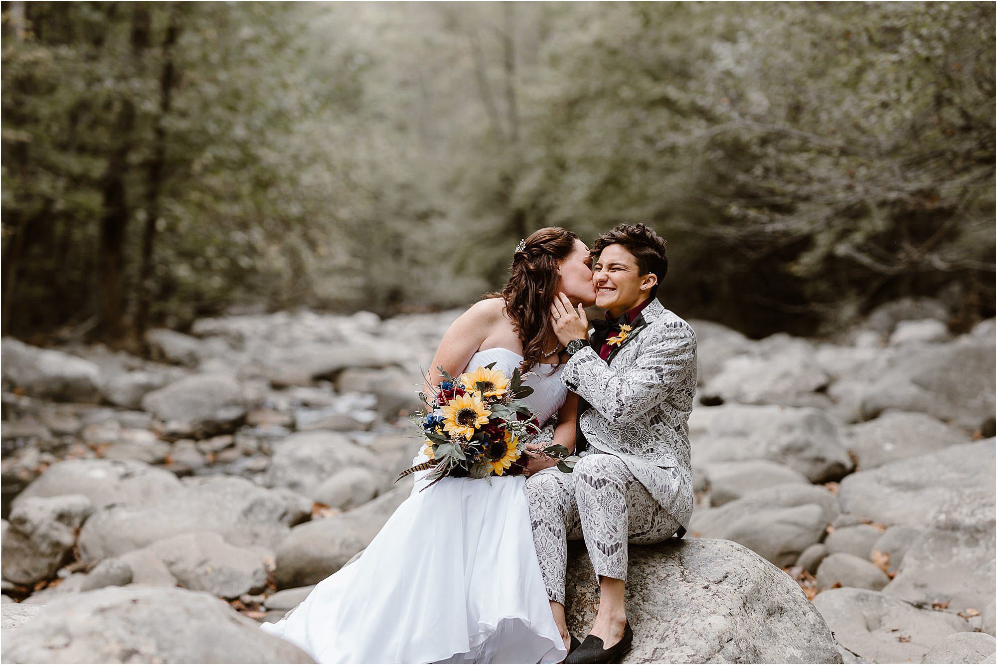 bride and bride kiss while sitting on rocks