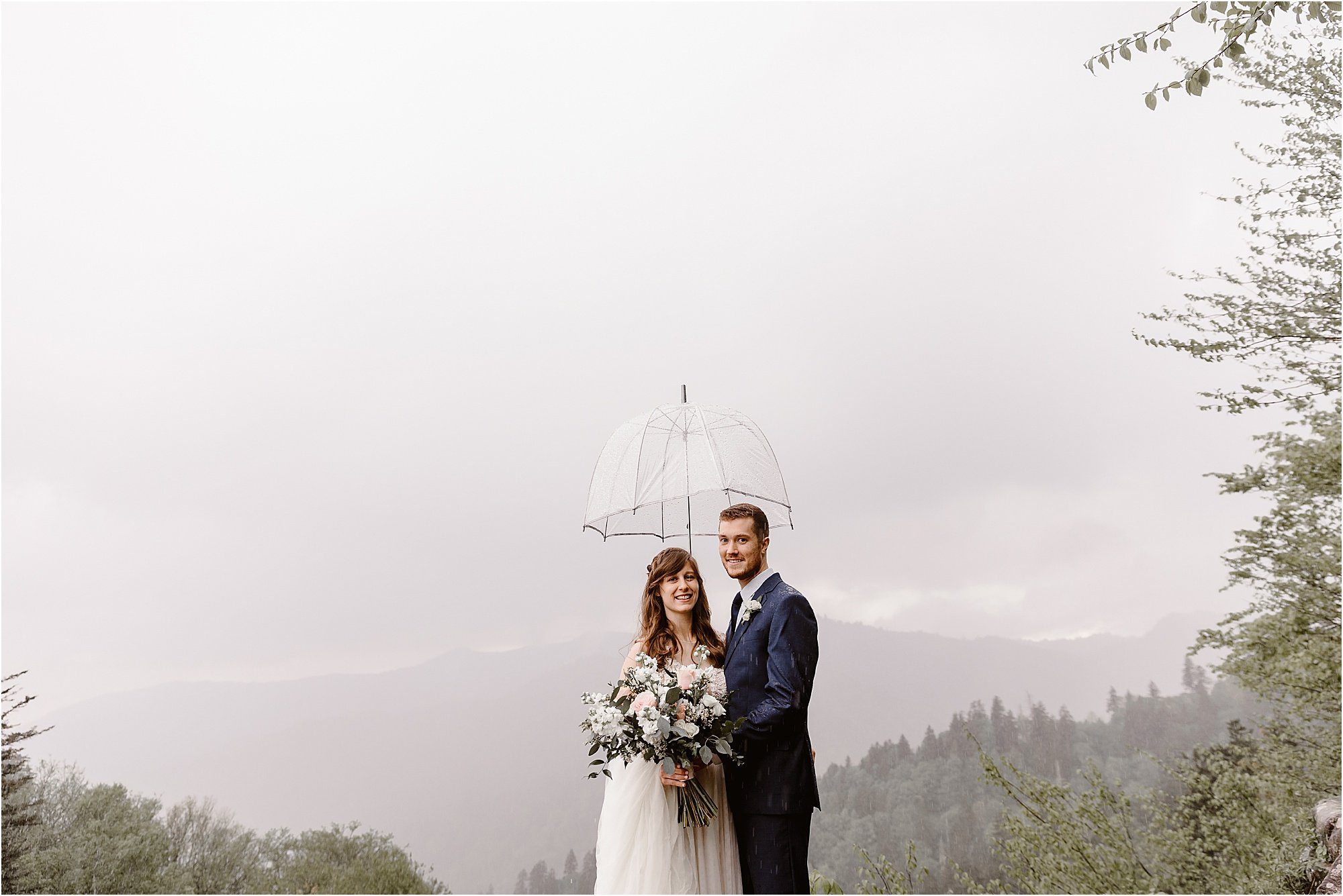 bride and groom stand under clear umbrella during rainy wedding day