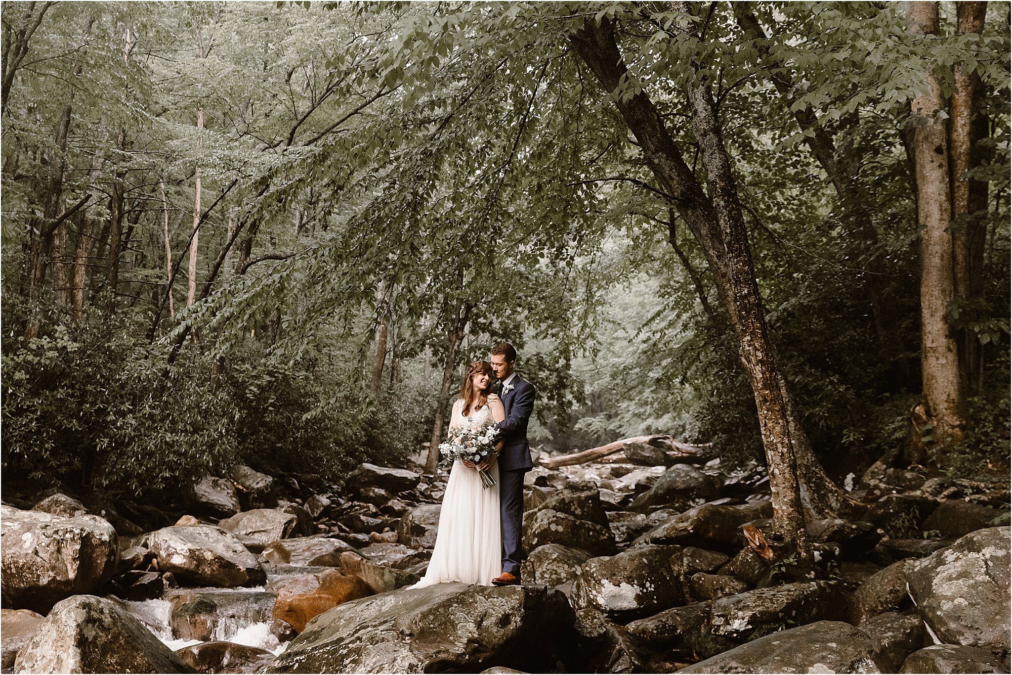 Bride and groom kiss while on the rocks of river