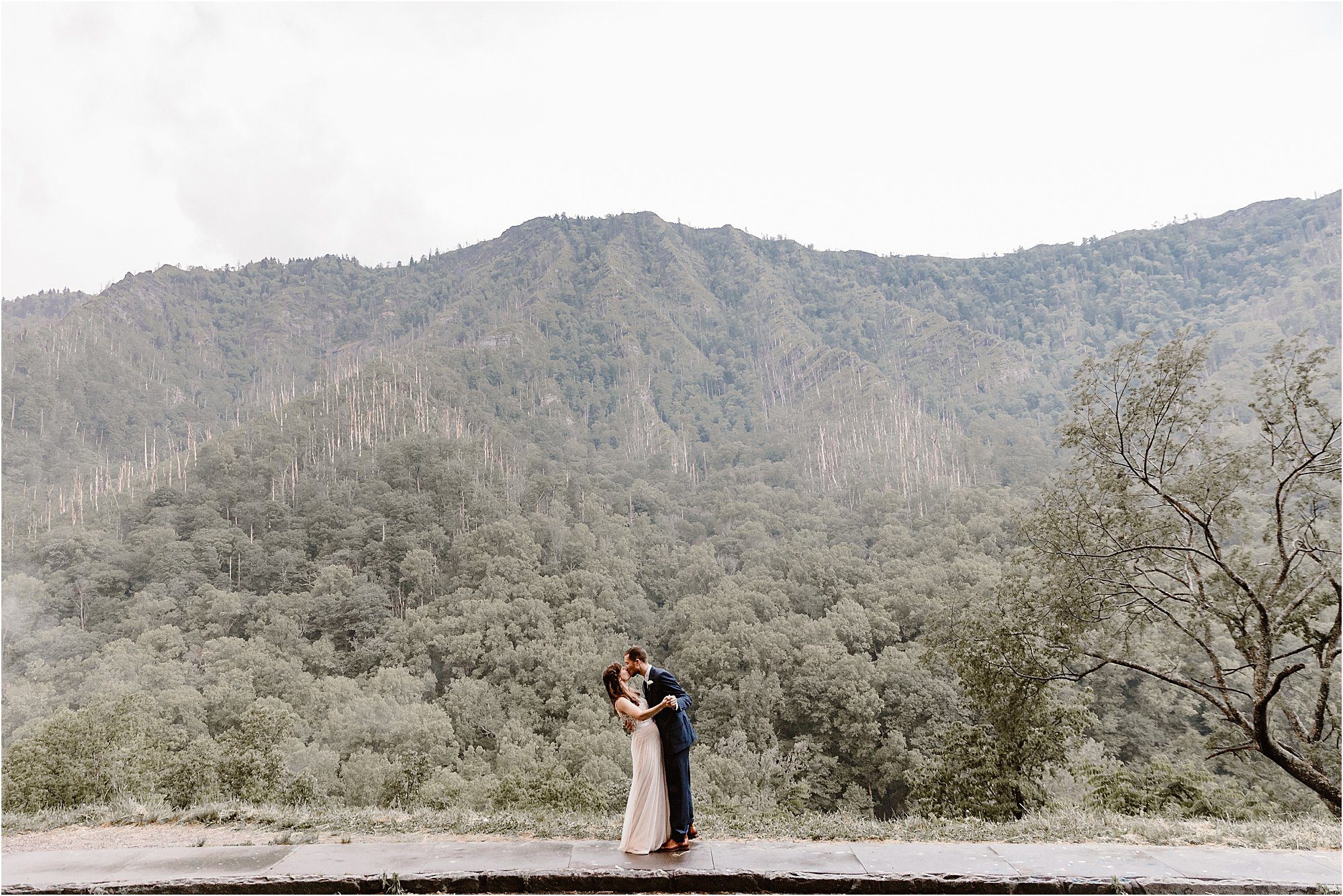 groom dips bride in front of mountain landscape