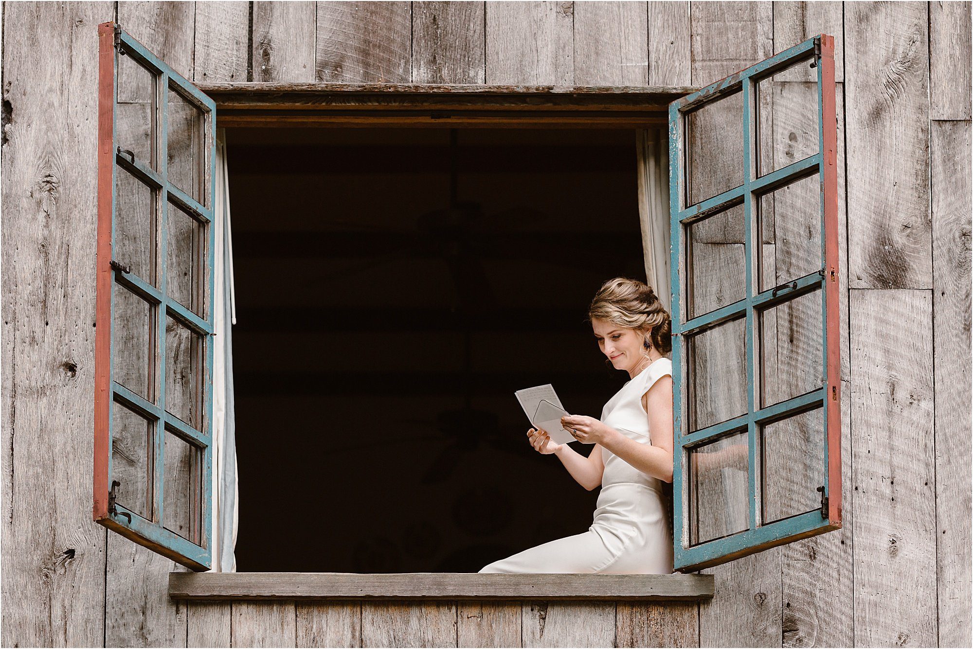 bride reads letter from groom while sitting in window