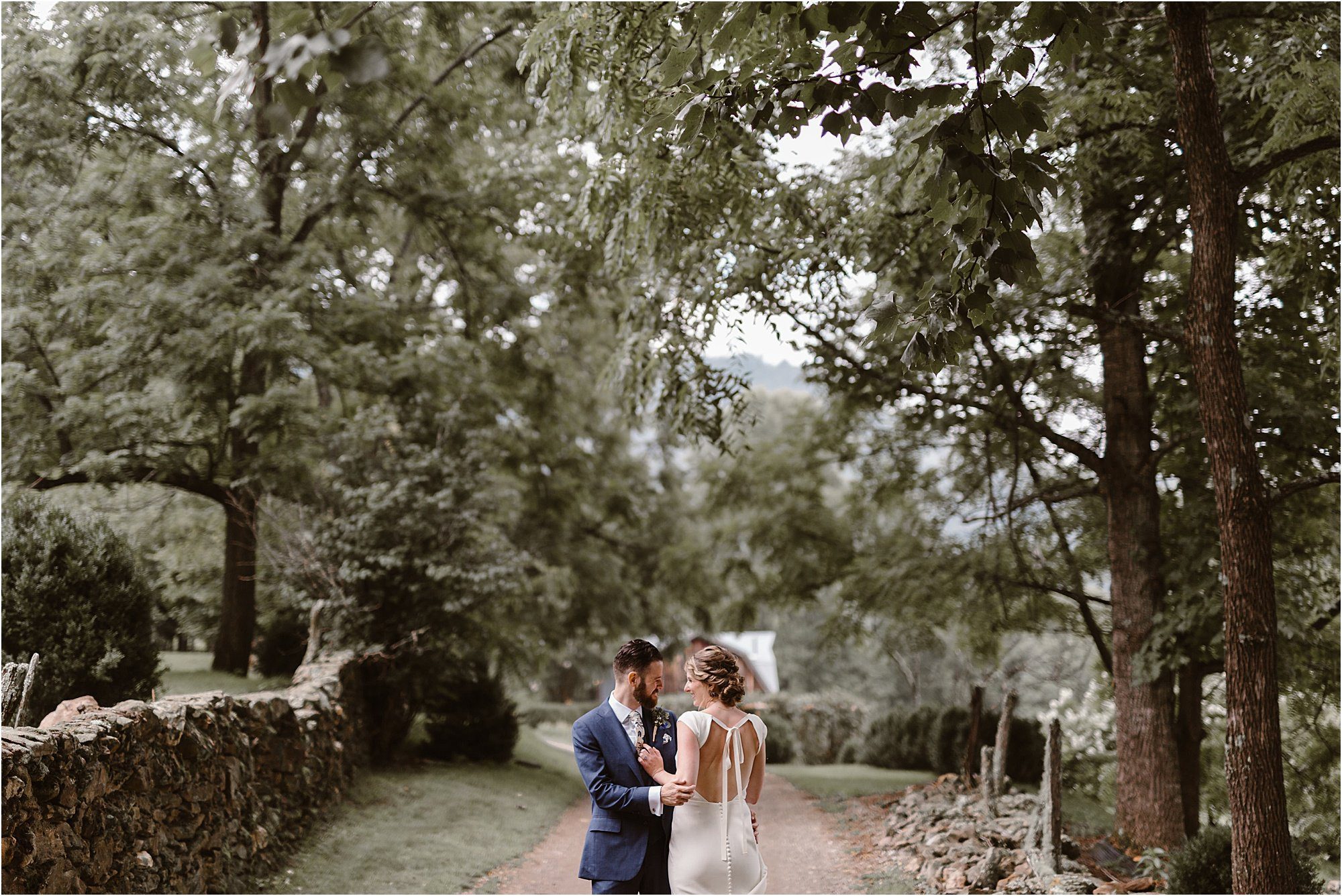 bride and groom kiss and hug while standing on dirt road in front of rustic barn