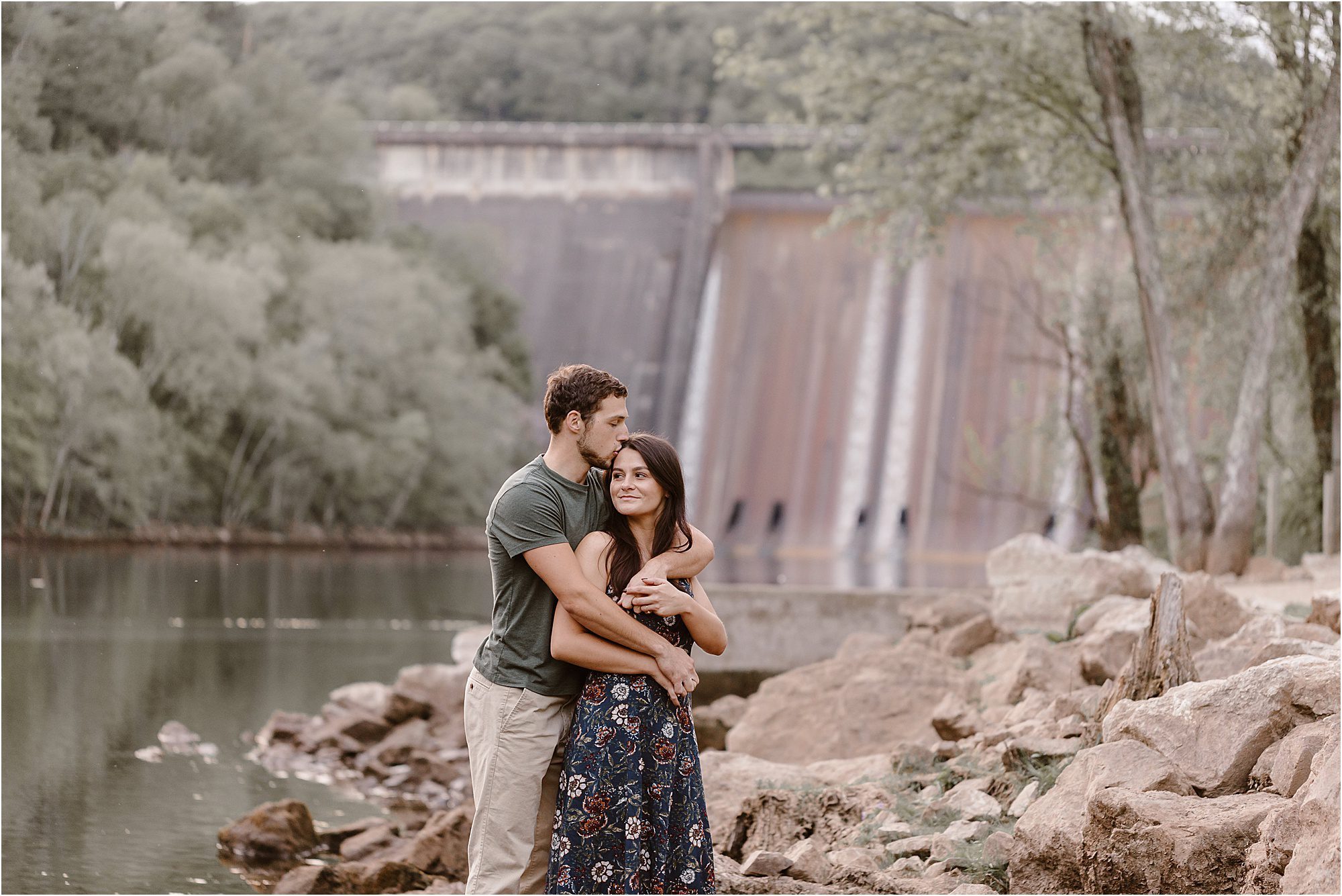 man hugs woman from behind in front of dam wall