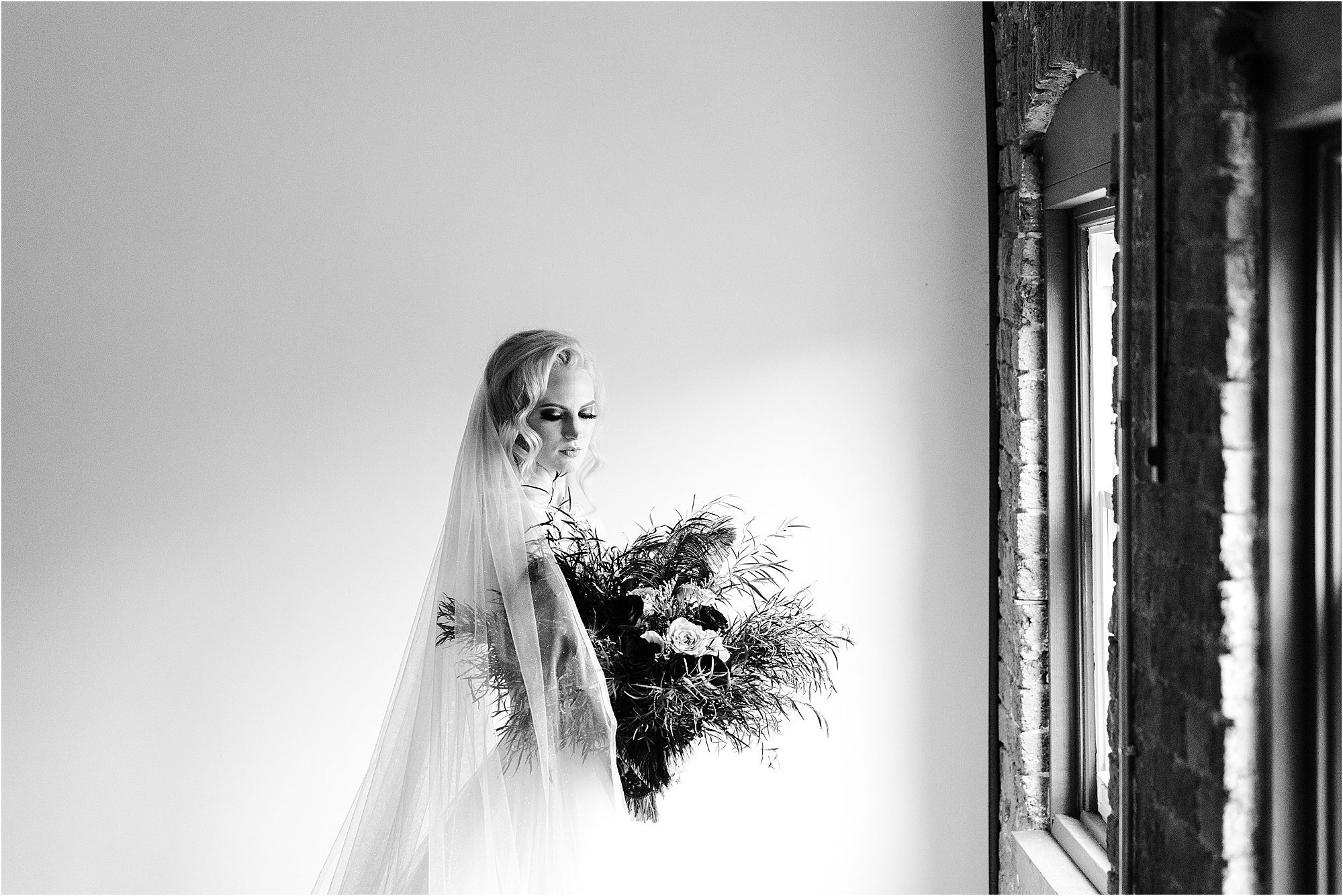 black and white bridal photo with long veil by window