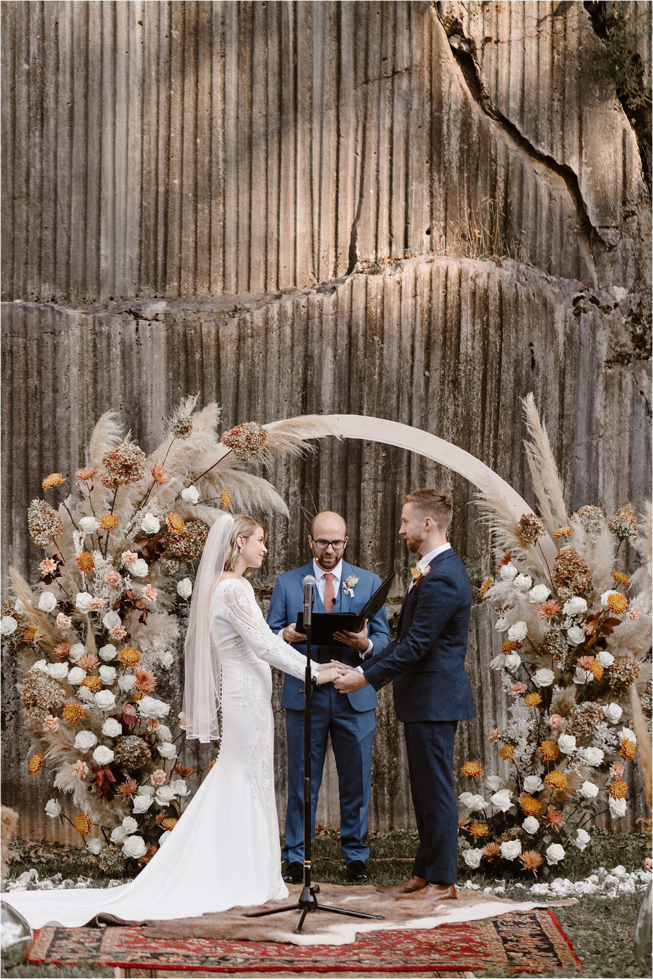 bride and groom standing in front of circular arbor at wedding ceremony surrounded by orange and cream flowers