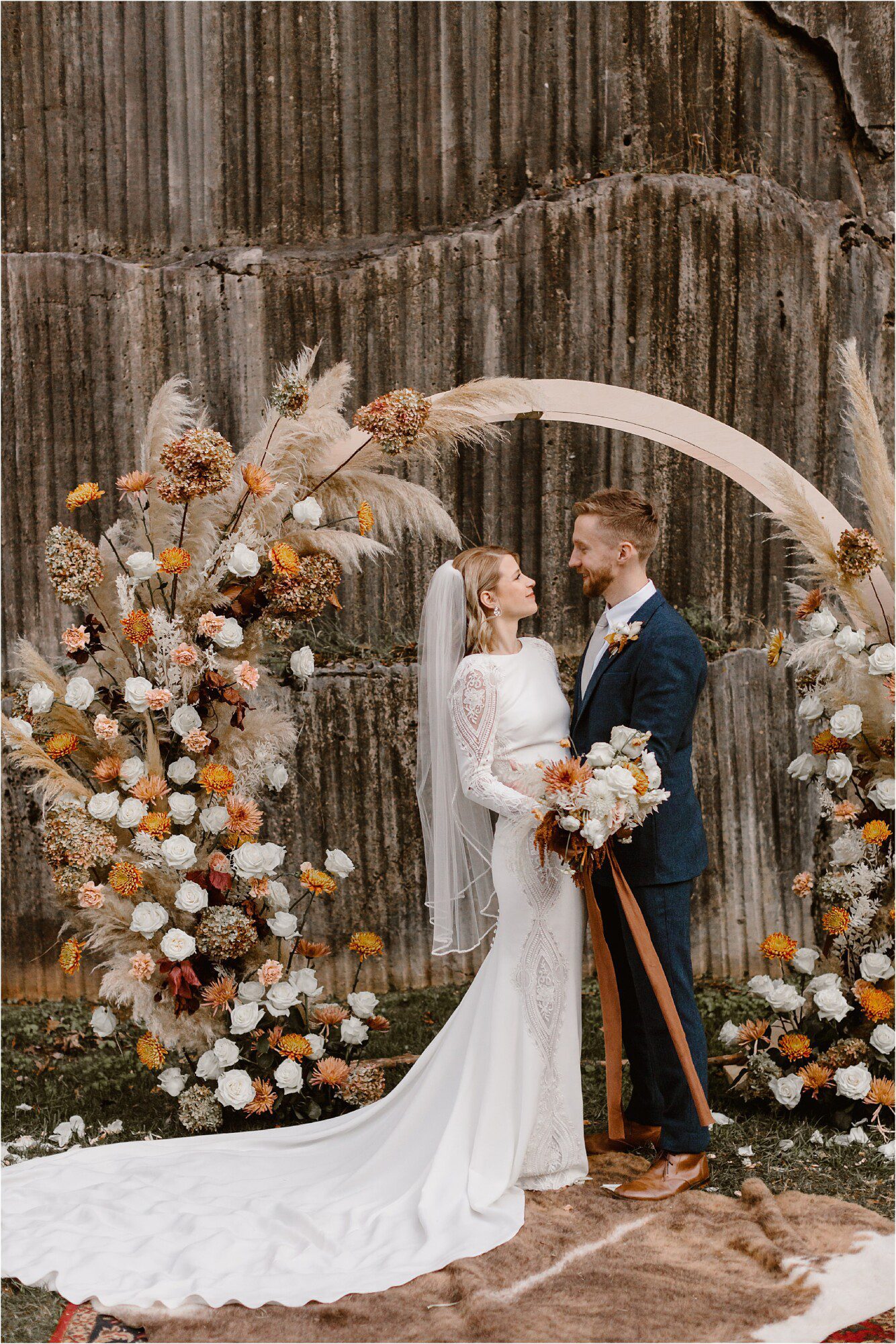 bride and groom stand in front of boho circle ceremony arbor at autumnal wedding