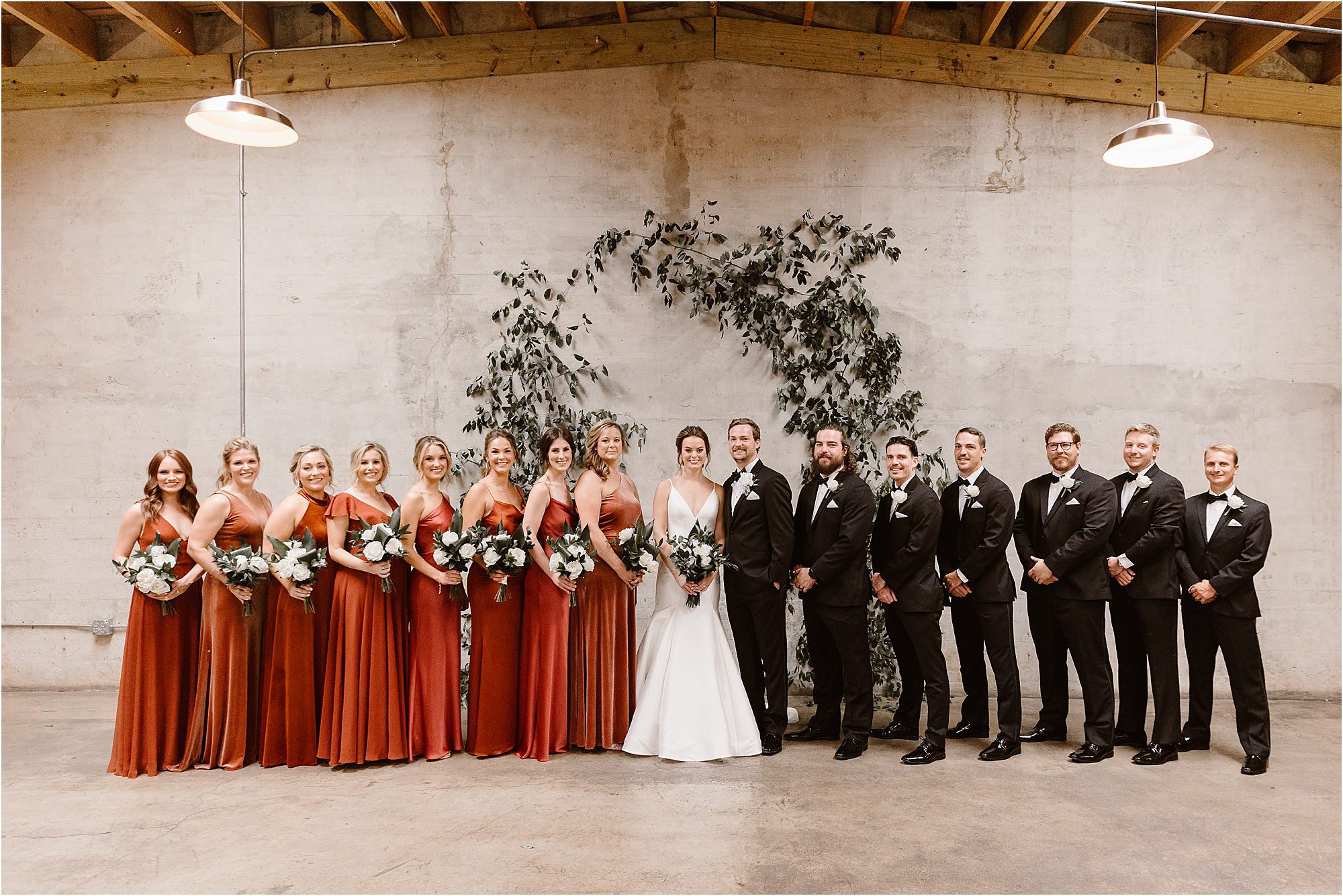 wedding party photos in front of greenery arbor and slate wall