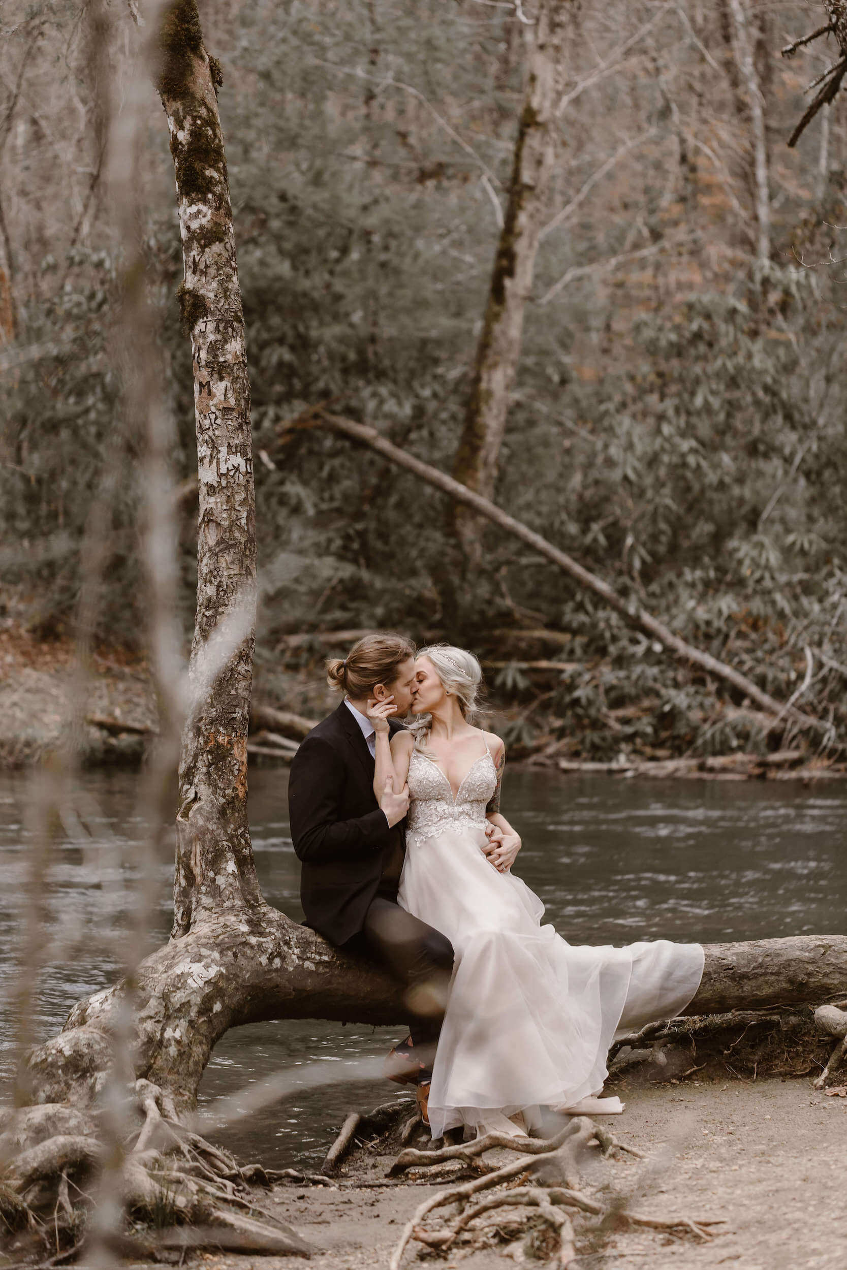 bride and groom kissing on log by stream