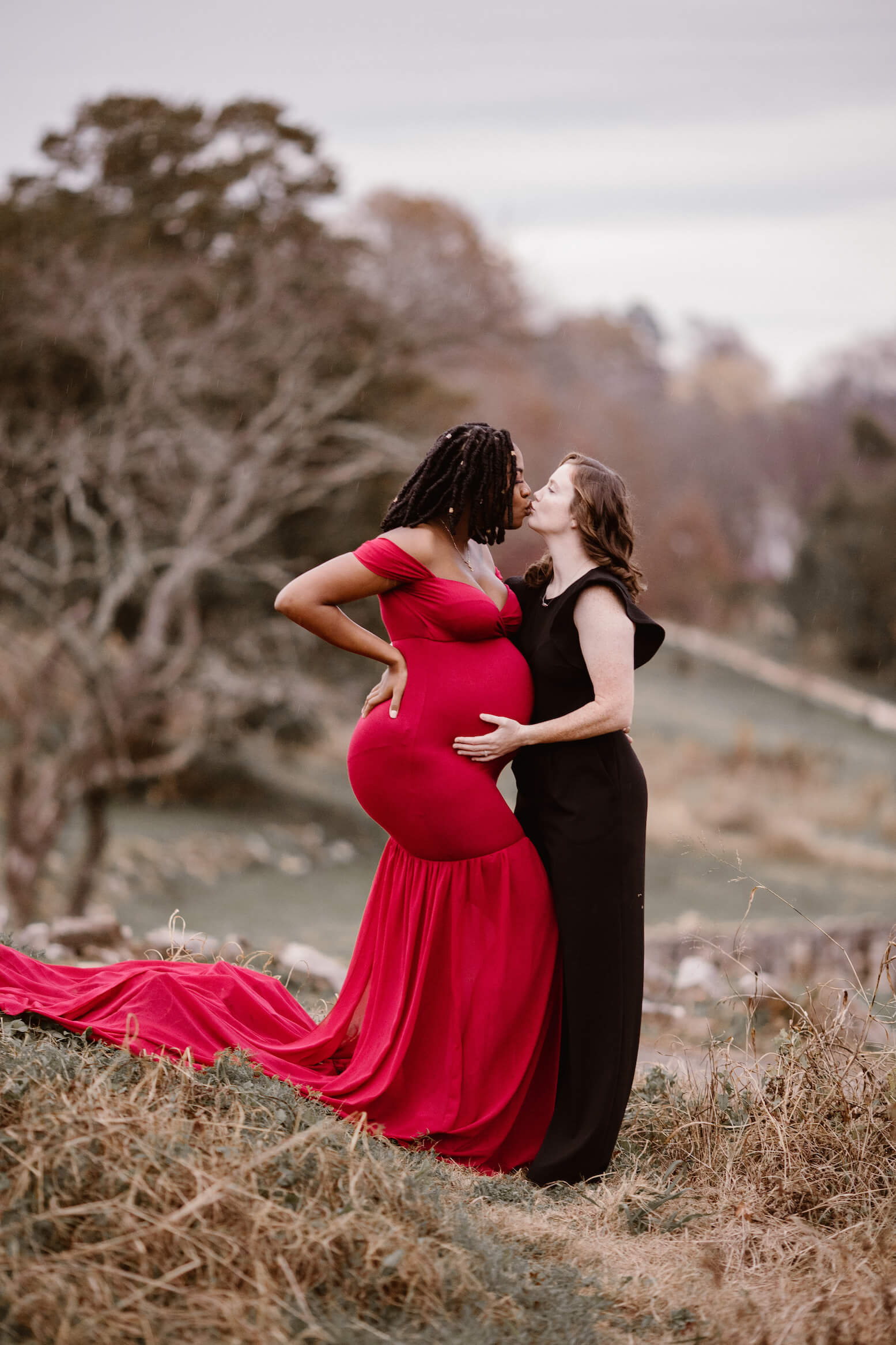 pregnant woman in red dress kissing woman in black dress during family photography session
