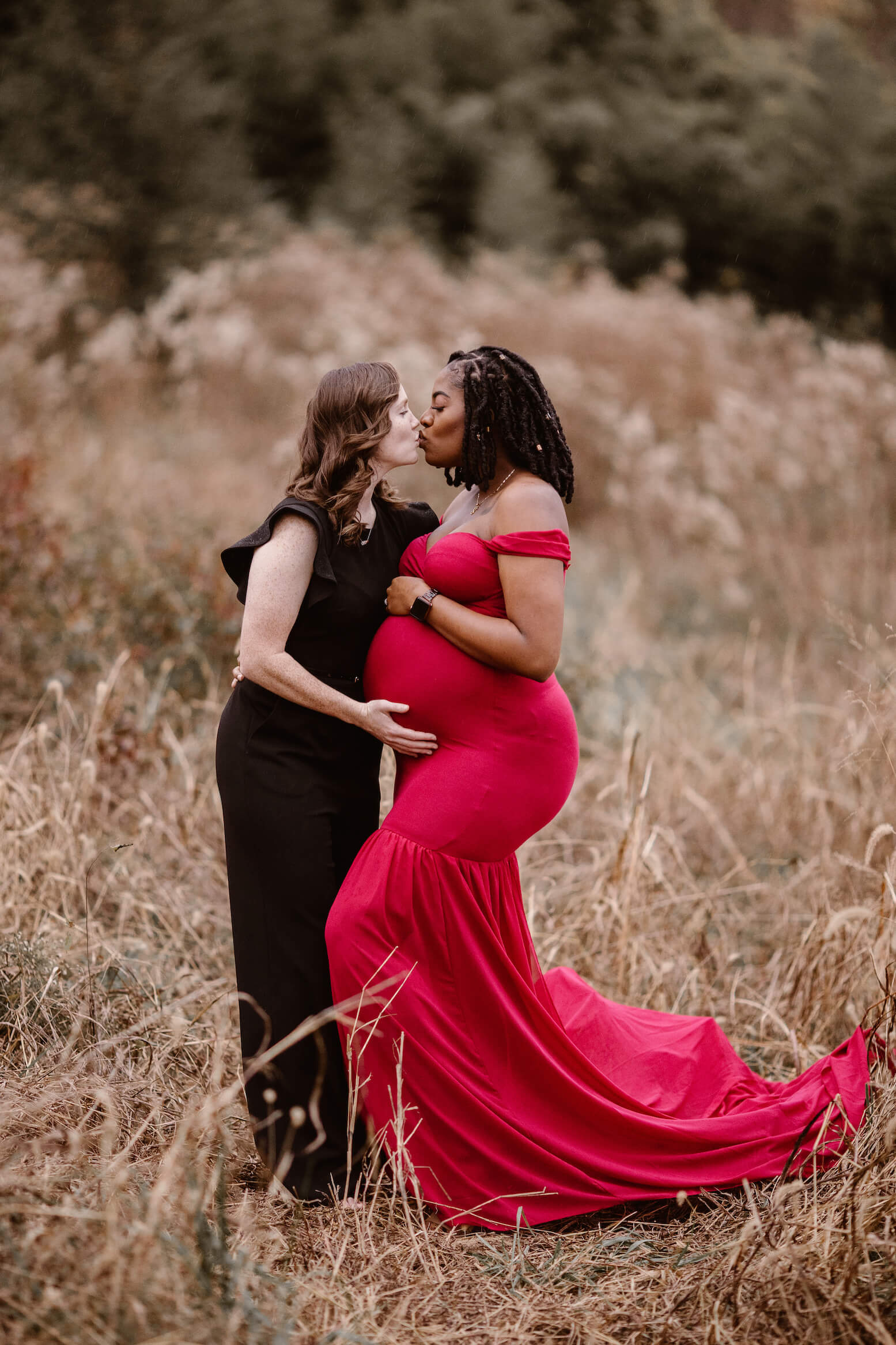 pregnant woman in red dress kissing woman in black dress