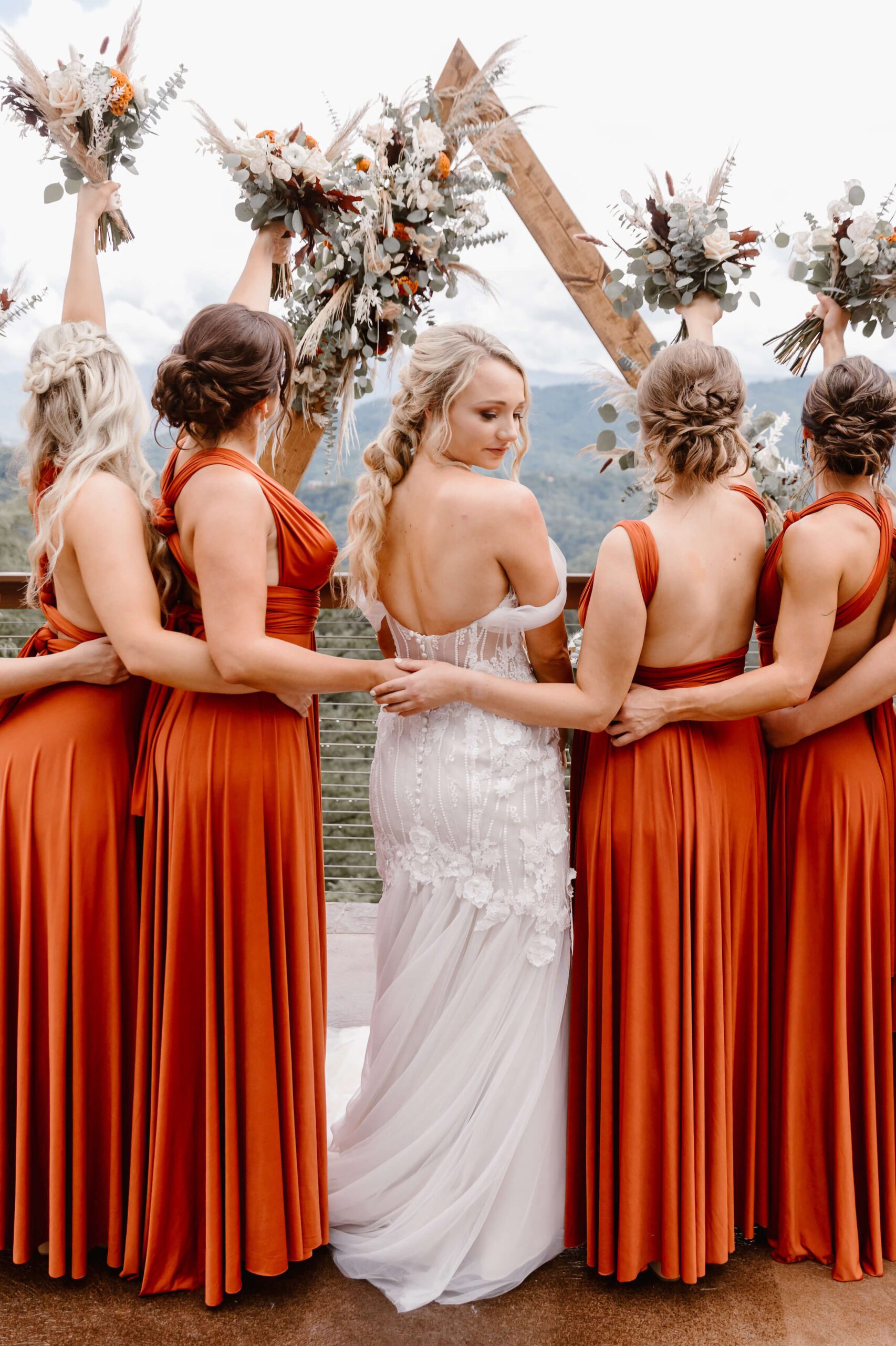bride looking over shoulder while bridesmaid toast their bouquets
