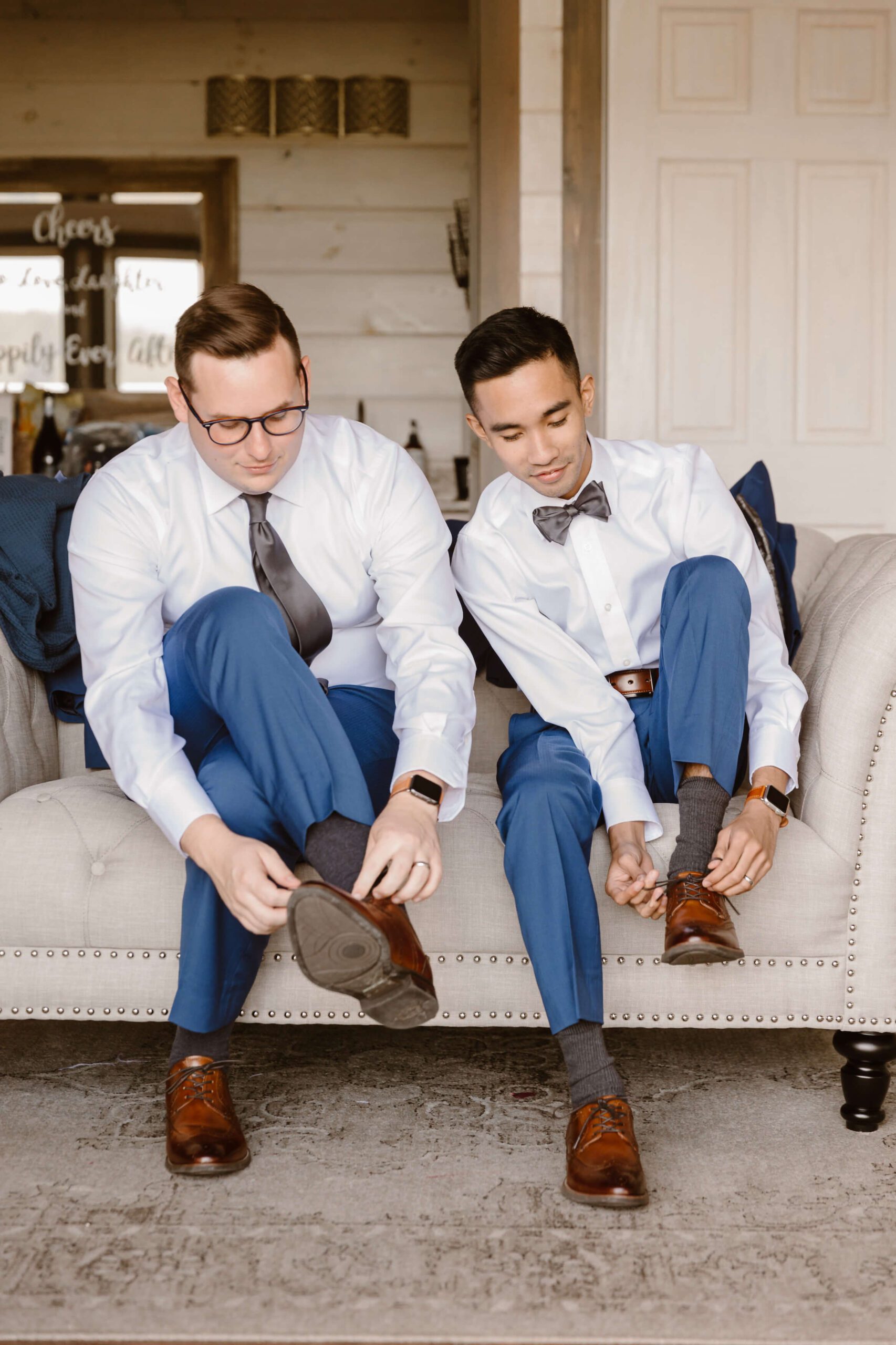 same sex wedding with two grooms tying brown shoes while sitting on couch