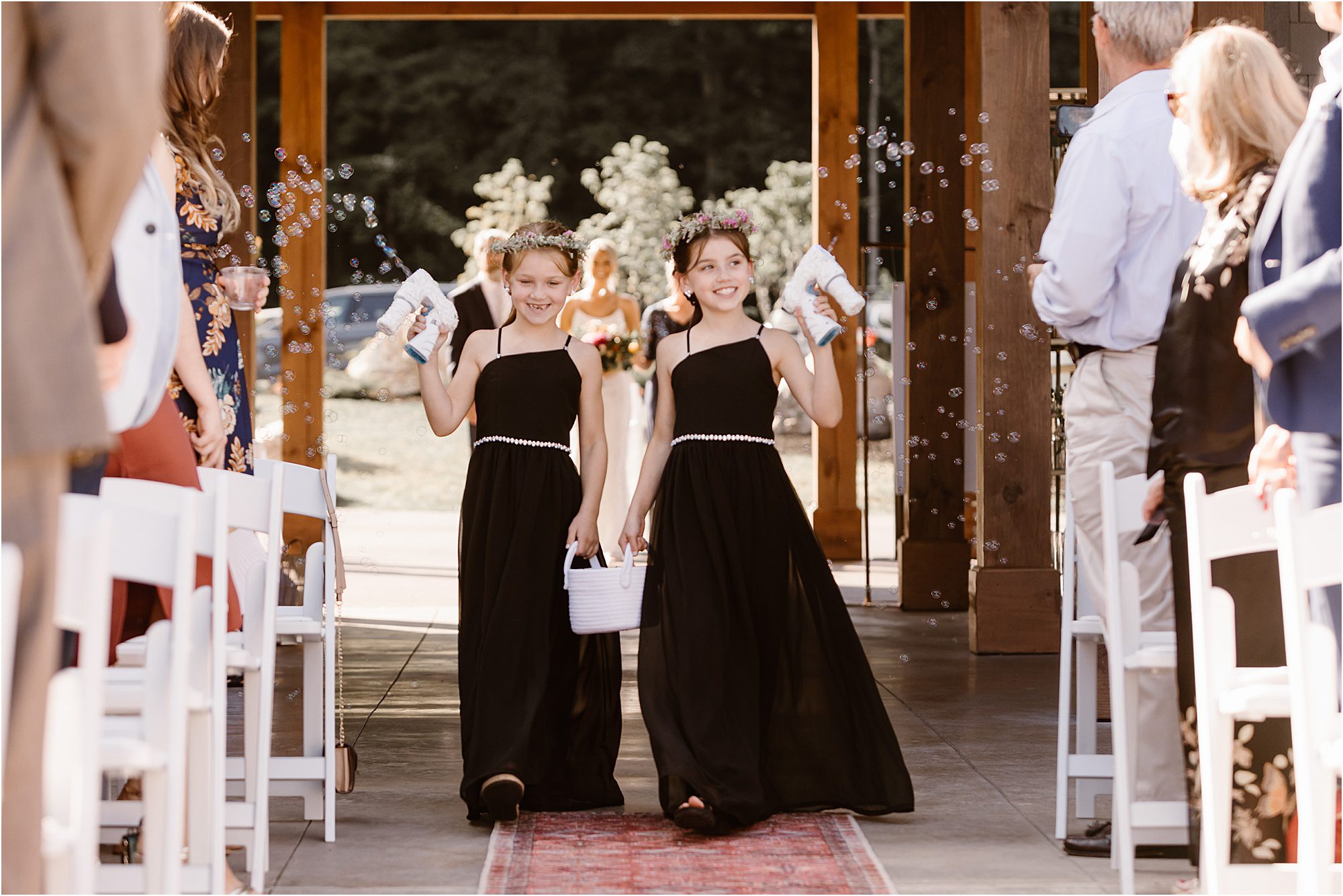 flower girls in black wedding dresses holding bubble guns down aisle