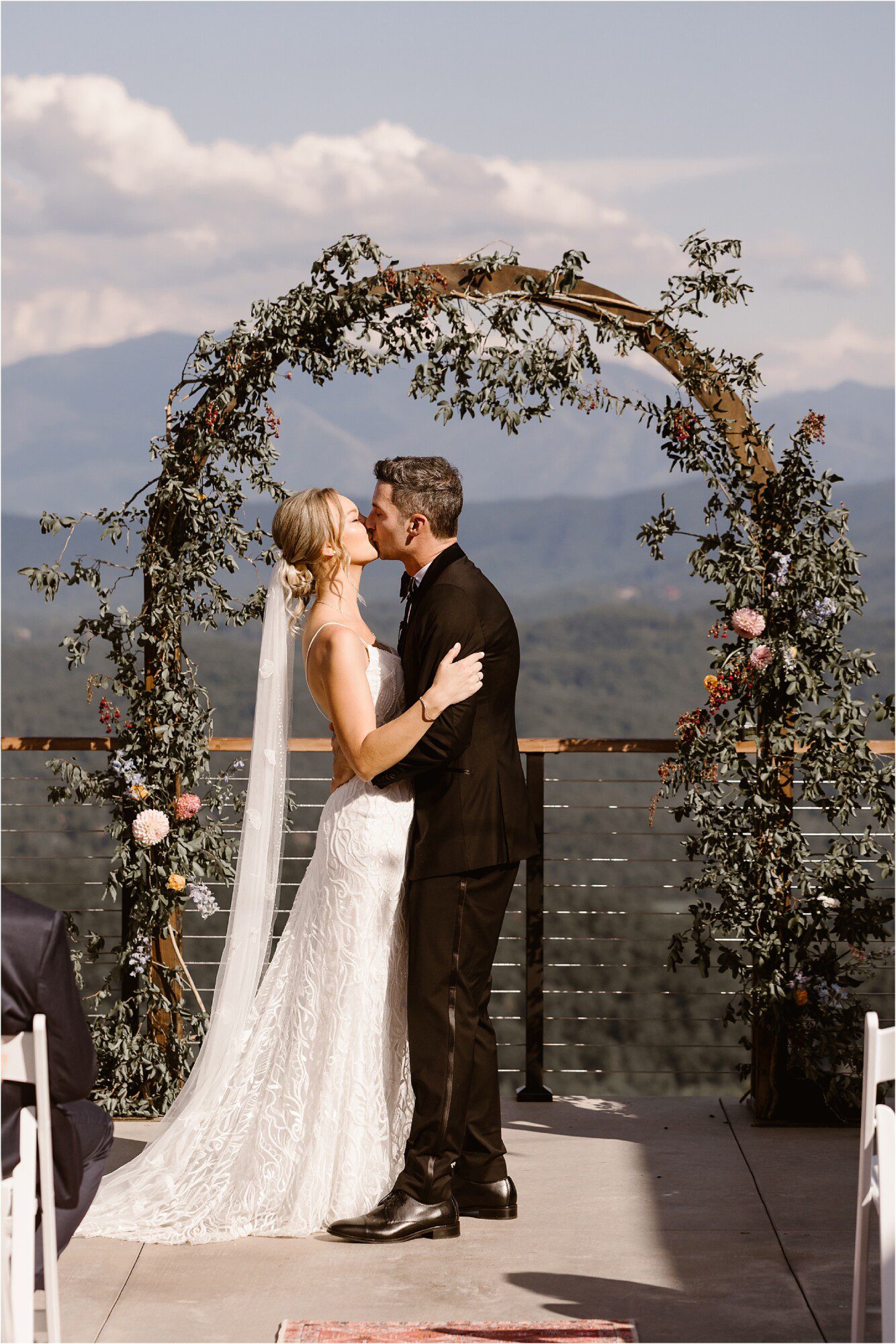 bride and groom kiss at wedding ceremony with floral arbor