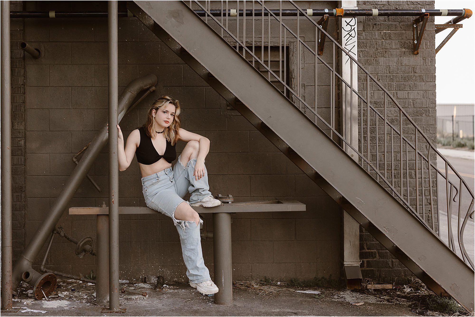 grunge senior photos with girl sitting under stairs in black top and light cut jeans