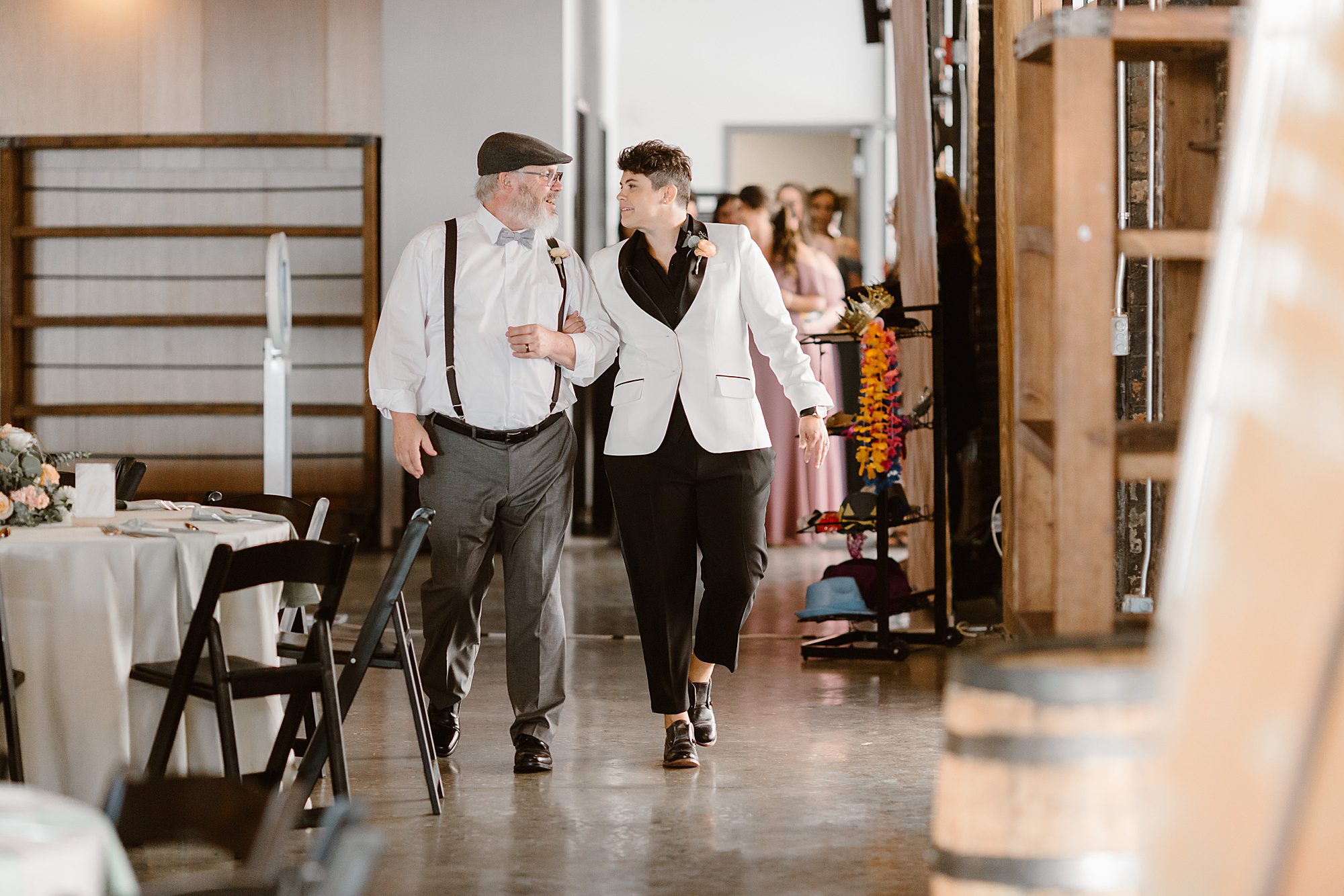 bride in black and white suit walks down aisle with father at intimate wedding
