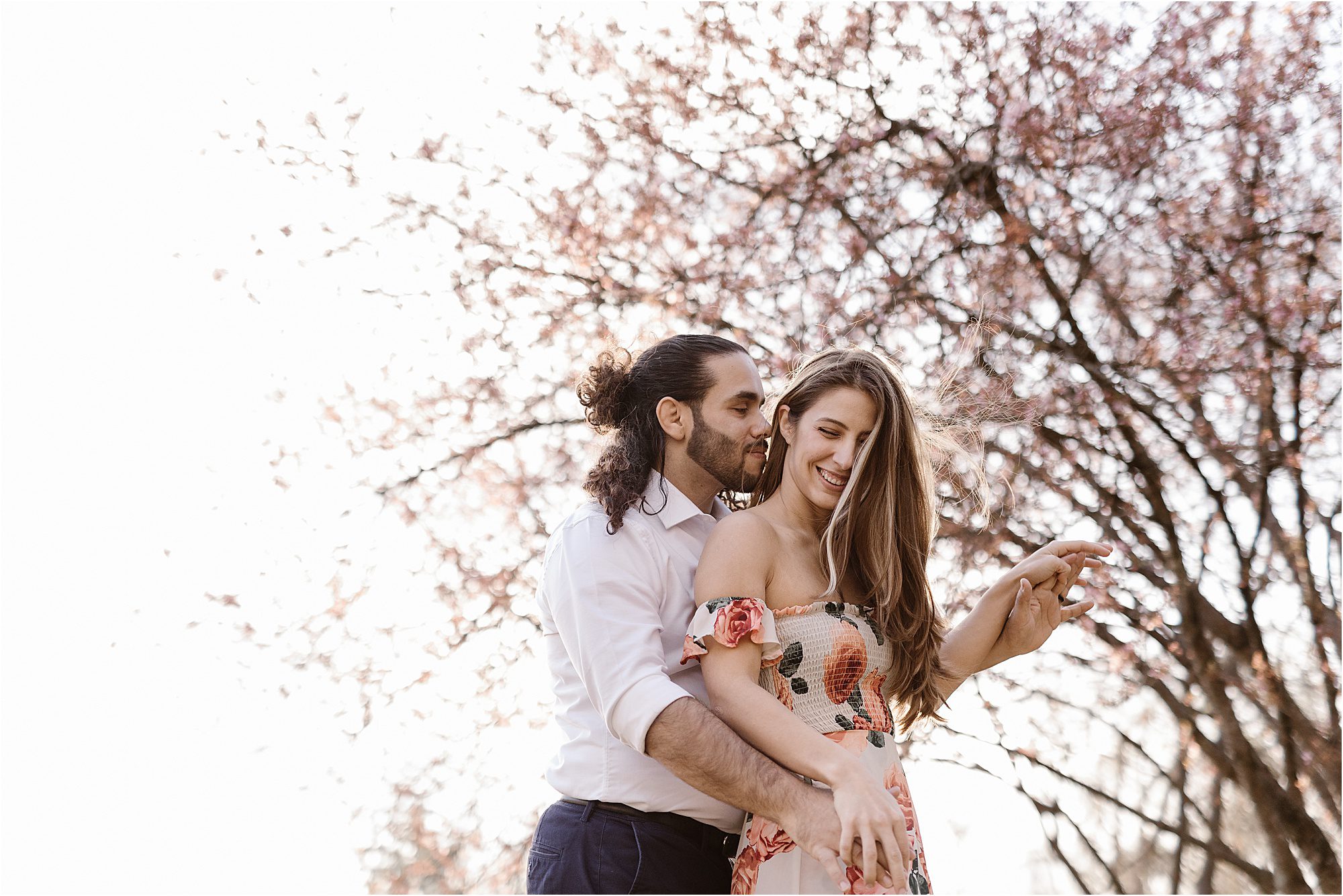 man and woman smiling and hugging while standing in front of flowering tree