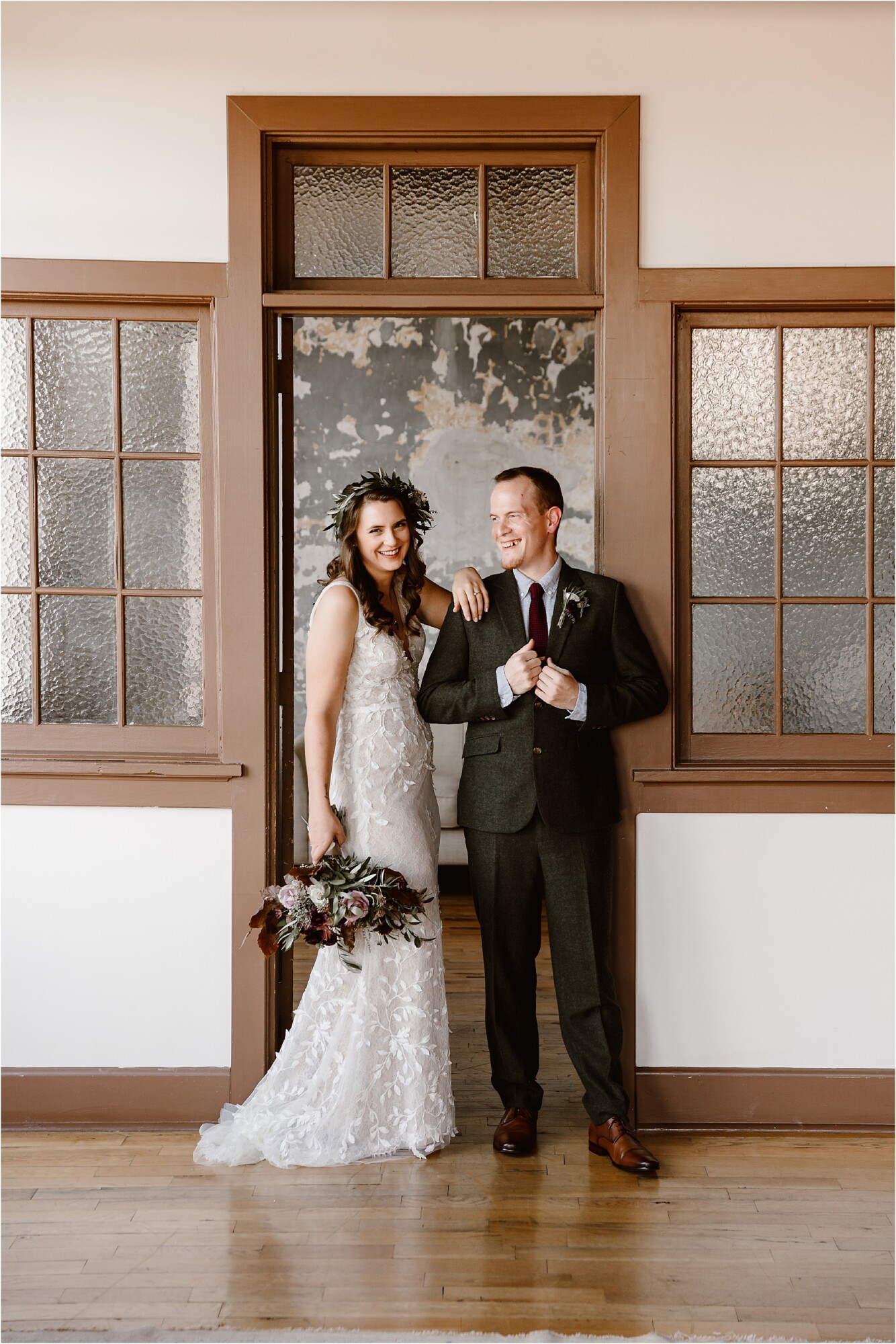 bride in flower crown and groom in tweed suit laugh together standing in front of vintage door