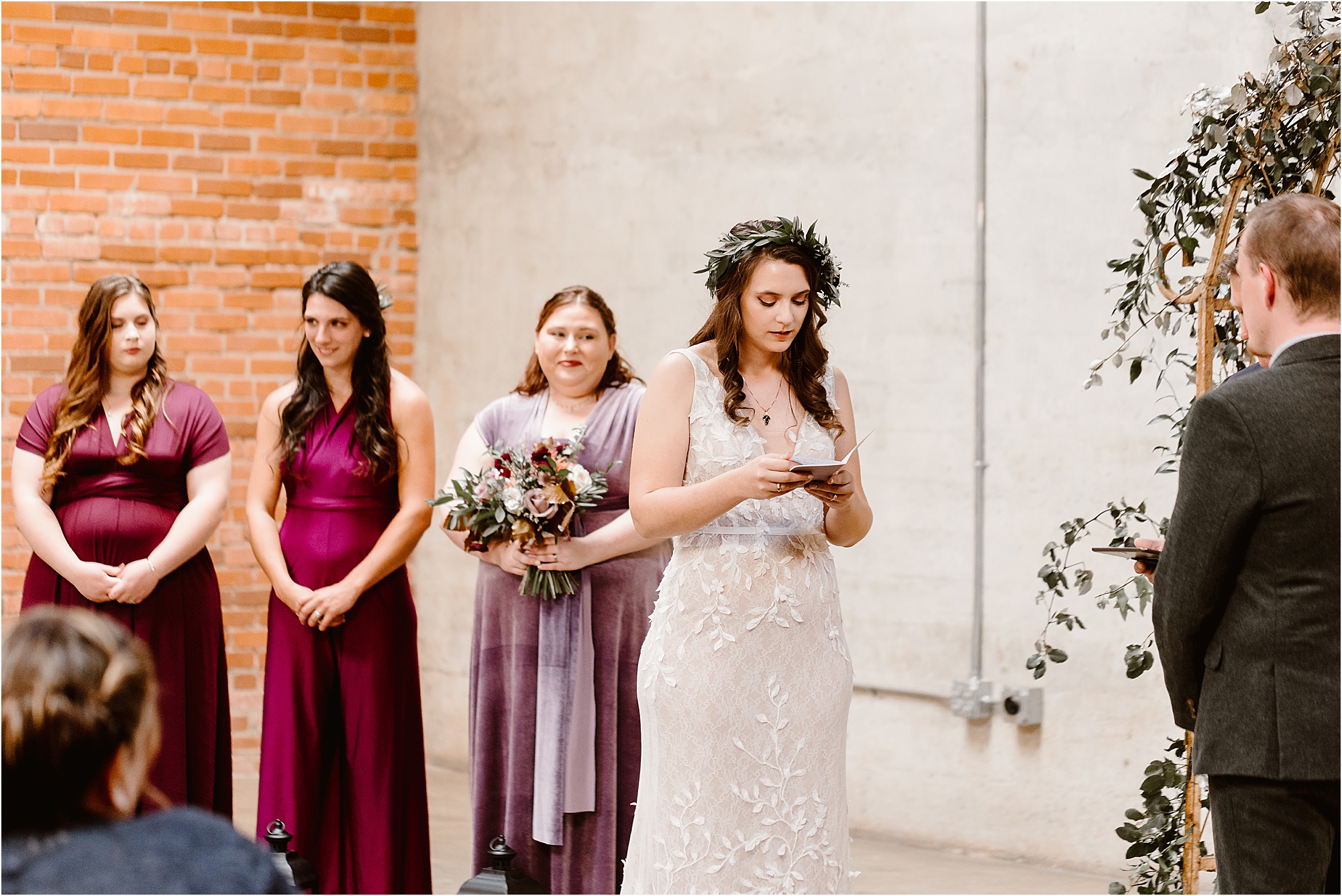 bride reads vows at wedding ceremony in front of bridesmaids in purple and burgundy dresses