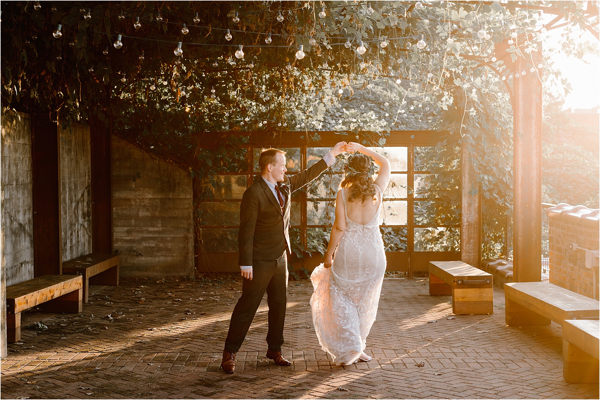 groom twirls bride at sunset on patio with hanging vines 